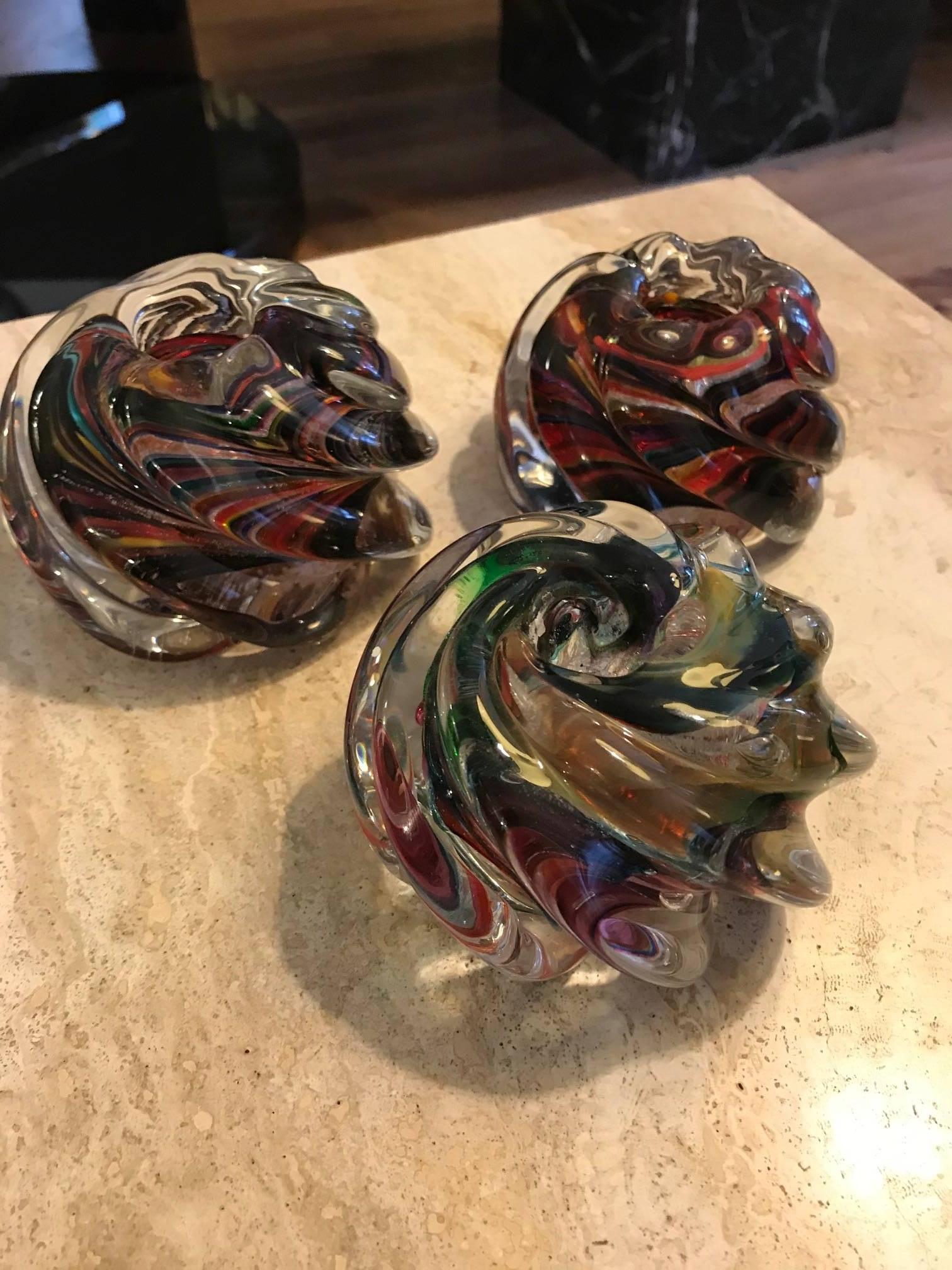 Three Murano glass votives. These candle holders have deep swirls and have colored glass inclusions.
They are signed however the signature is not legible. Fine decorative tabletop objects.
Each votive is a slightly different size.