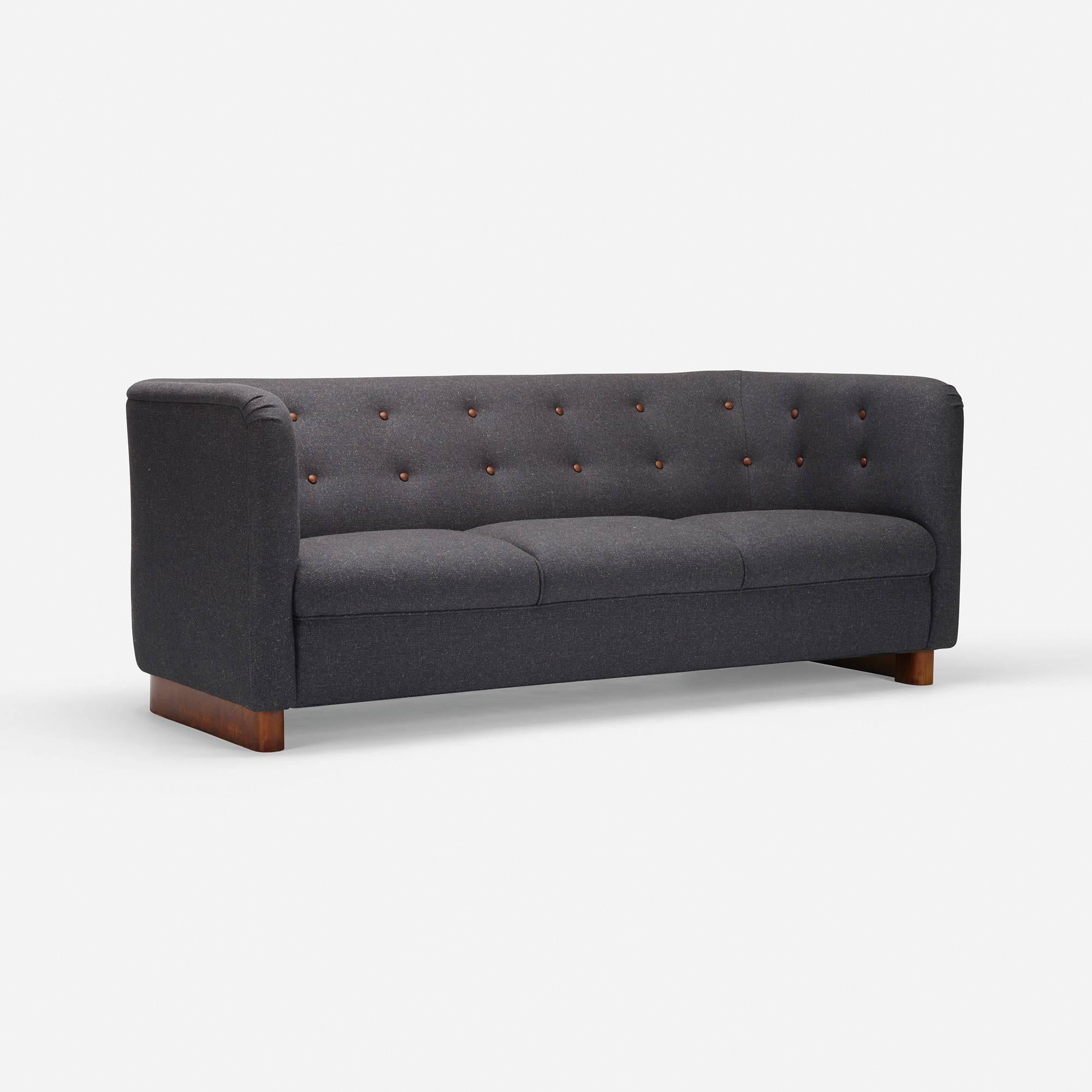 This elegant tuxedo style sofa has been recently updated in a fine menswear inspired wool with a light checked texture and faint melange. The piece is set off with dark brown leather buttons which tie back to the color of sofa's stylish curved base.