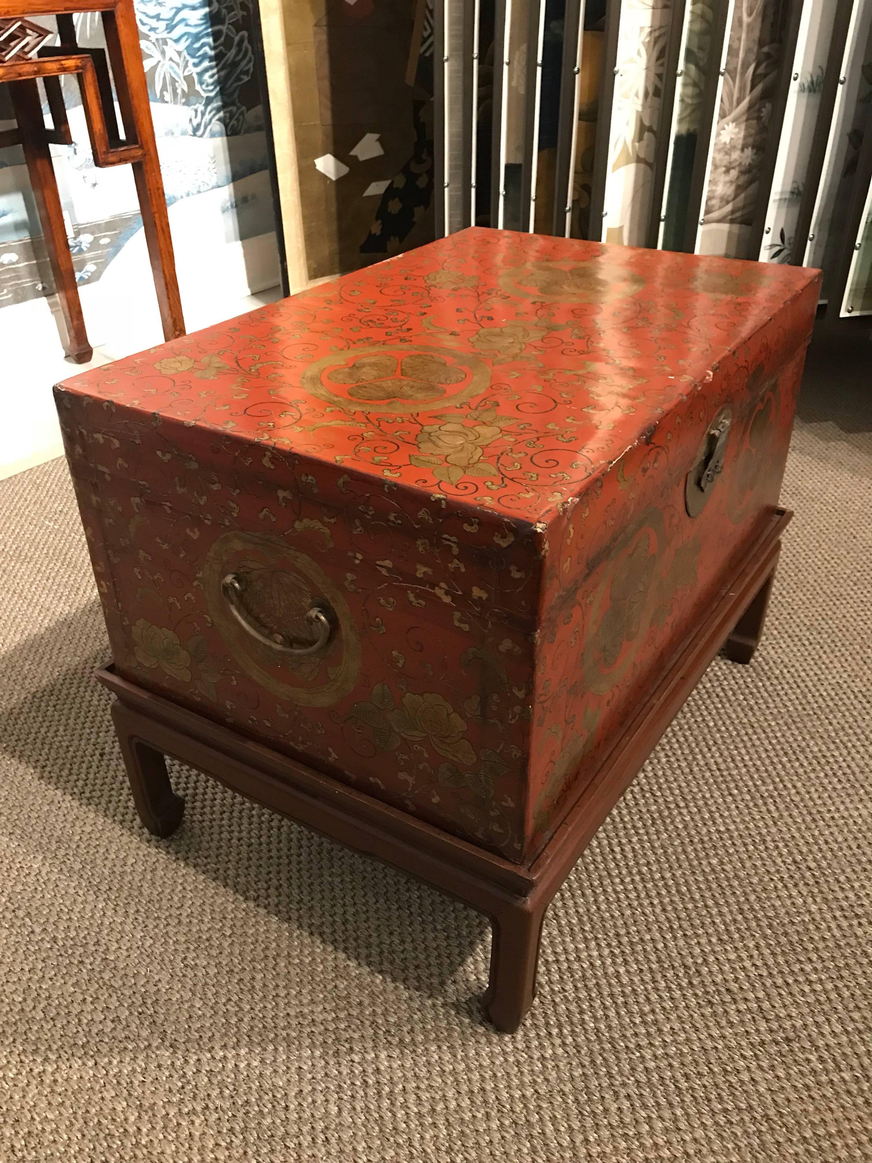 Chinese red leather trunk, circa 1920. This trunk is very decorative and unusual, since the gold design on the outside is Japanese crests and vines. 

On wooden stand. Height listed is total height on stand.