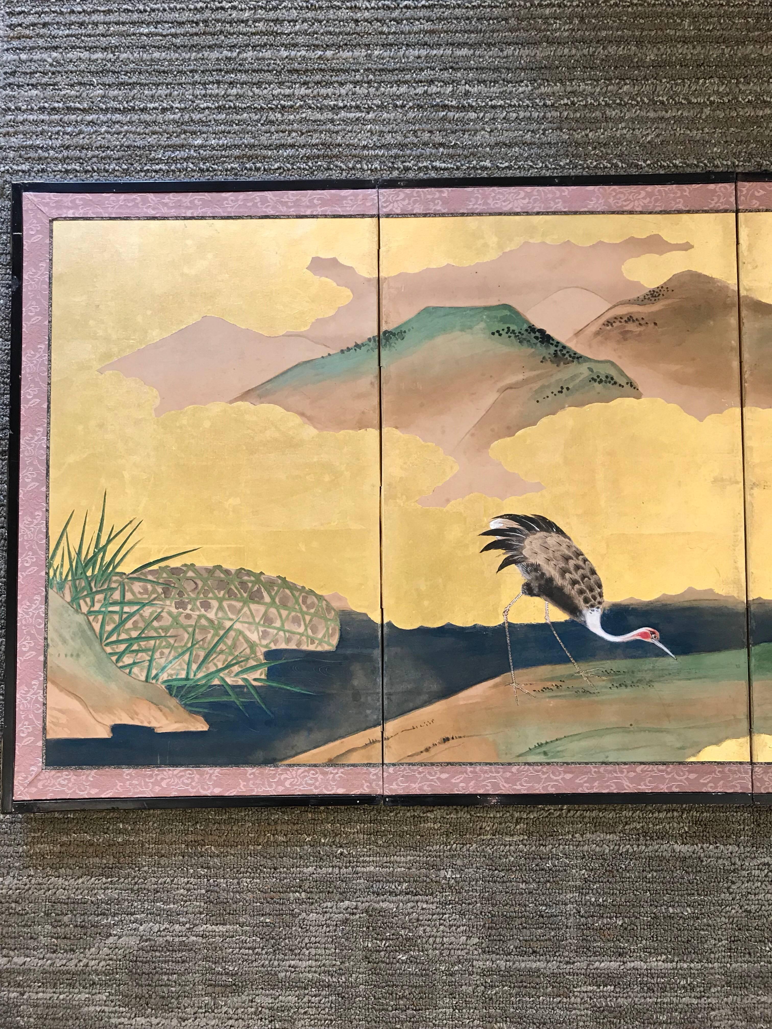 A six fold Japanese screen with pine trees, cranes, and bamboo on a gold leaf background, early 20th century.