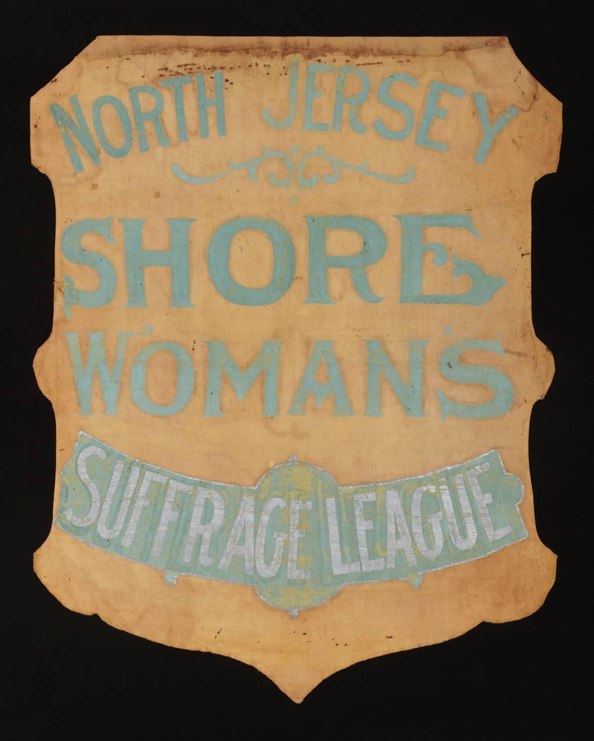Shield-shaped banner from the North Jersey shore woman's suffrage league, handed down through the family of its president, viola aguero, with a large archive of material that includes an image of her actually holding the banner:

 During the