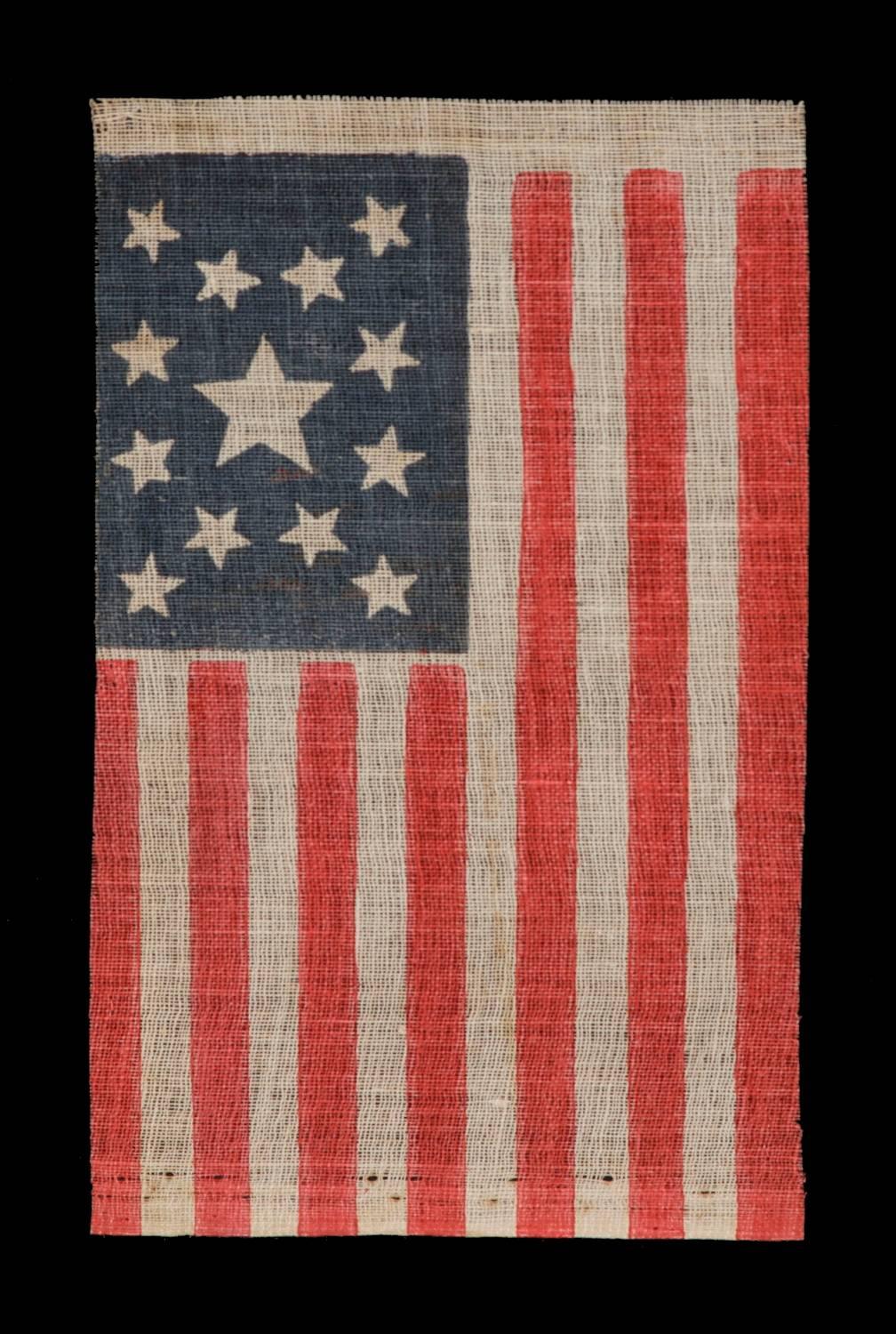 13 star American national parade flag, printed on coarse, glazed cotton, made for the 1876 celebration of our nation’s 100-year anniversary of independence. The stars are arranged in a medallion that consists of a star in the very center, surrounded