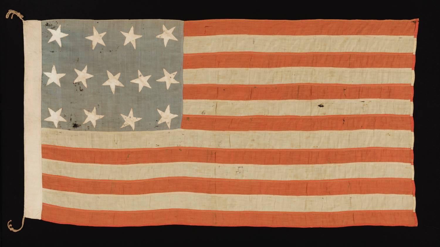 13 STARS IN A 4-5-4 PATTERN, ON AN ANTIQUE AMERICAN FLAG OF THE CIVIL WAR ERA, WITH BEAUTIFUL COLORATION AND IN A TINY SCALE AMONGST ITS PIECED-AND-SEWN COUNTERPARTS:

Made around the time of the American Civil War (1861-65), this American national