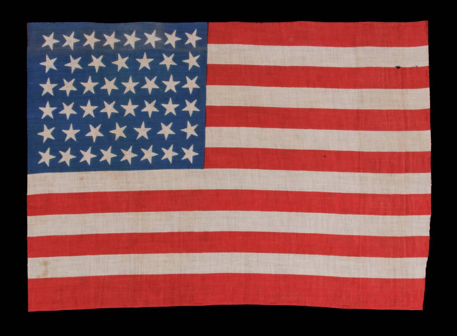 46 STARS ON A BRILLIANT ROYAL BLUE CANTON, ON AN ANTIQUE AMERICAN FLAG OF THE 1907-1912 PERIOD, OKLAHOMA STATEHOOD, SCATTERED STAR POSITIONING: 

46 star American parade flag, printed on cotton. The stars are arranged in a rectilinear fashion, but
