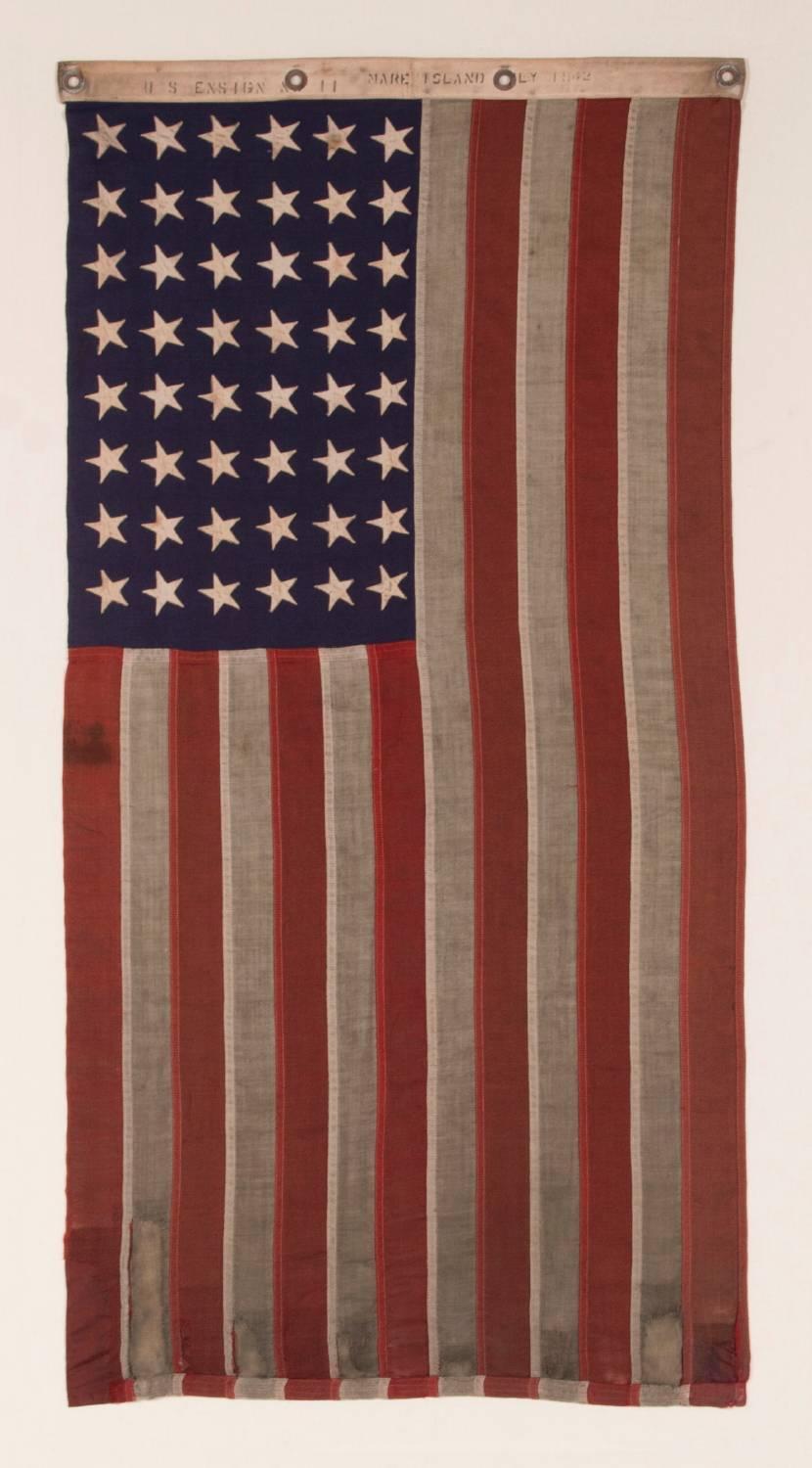 48 STAR, U.S. NAVY SMALL BOAT ENSIGN, MADE AT MARE ISLAND, CALIFORNIA [HEADQUARTERS OF THE PACIFIC FLEET] DURING WWII, SIGNED AND DATED JULY 1942, WITH EXTENSIVE WEAR FROM OBVIOUS USE:

48 star American national flag, made during World War II (U.S.