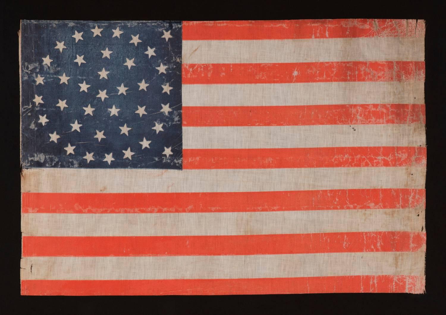 38 STARS IN A BEAUTIFUL MEDALLION CONFIGURATION WITH 2 OUTLIERS, ON A LARGE SCALE ANTIQUE AMERICAN PARADE FLAG OF THE 1876-1889 ERA, COLORADO STATEHOOD: 

38 star American parade flag, block-printed by hand on coarse, glazed cotton. The stars are