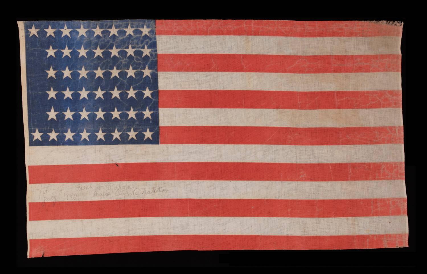 44 STARS IN A NOTCHED PATTERN ON A LARGE AMERICAN PARADE FLAG WITH A PENCILED INSCRIPTION FROM A CELEBRATION OF JULY 4TH IN NORTH DAKOTA, 1890-1896, REFLECTS WYOMING STATEHOOD, EX-RICHARD PIERCE COLLECTION: 

44 star American parade flag, printed on