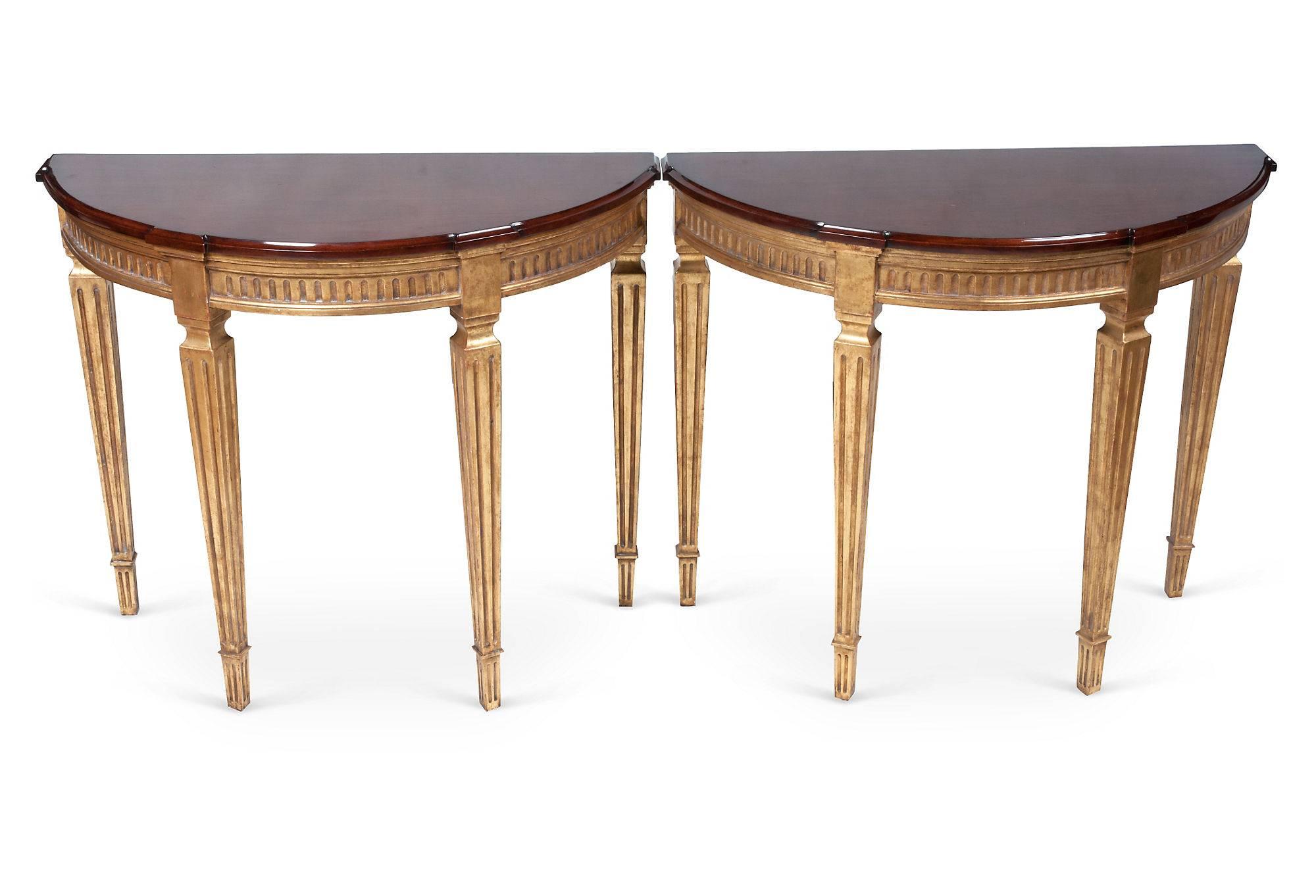 A pair of demilune tables with gold bases and cherrywood tops.