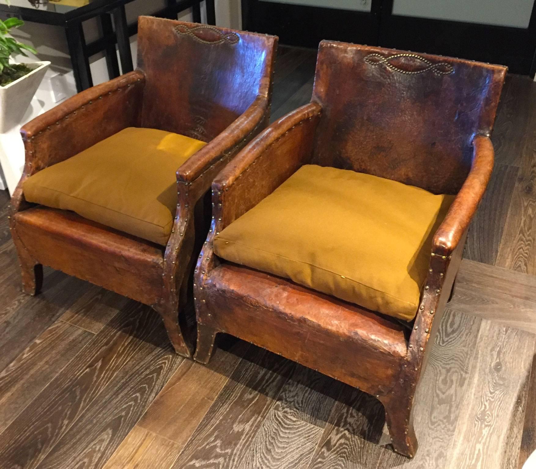 A pair of French leather chairs with mustard colored seat cushions. The chairs were made in 1930, and have beautiful nailhead detailing throughout.