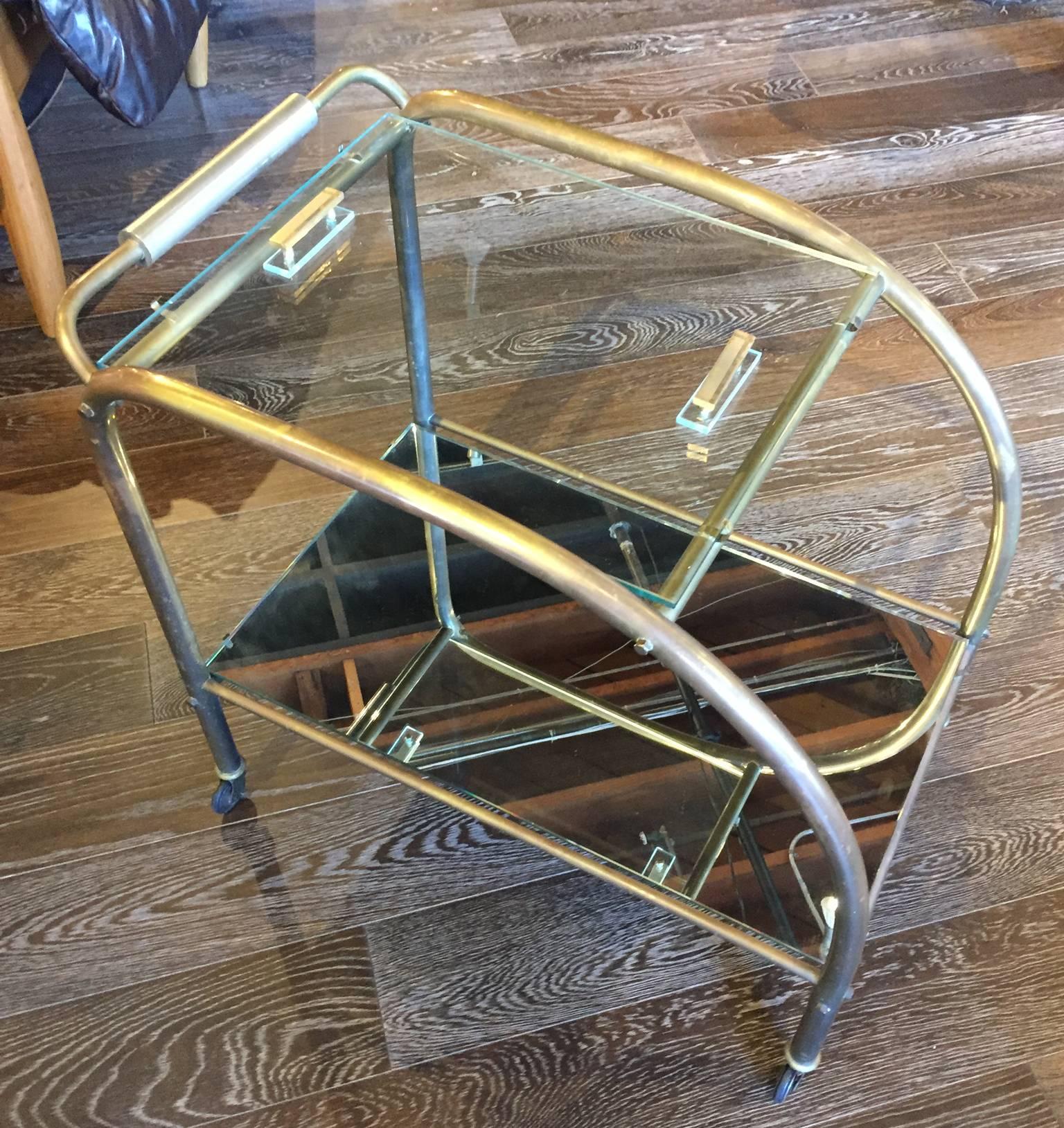 Beautiful bar cart in antiqued brass with a chrome handle. Top glass piece has handles to use for serving. Bottom glass tier is mirrored. Cart on wheels. In good condition.