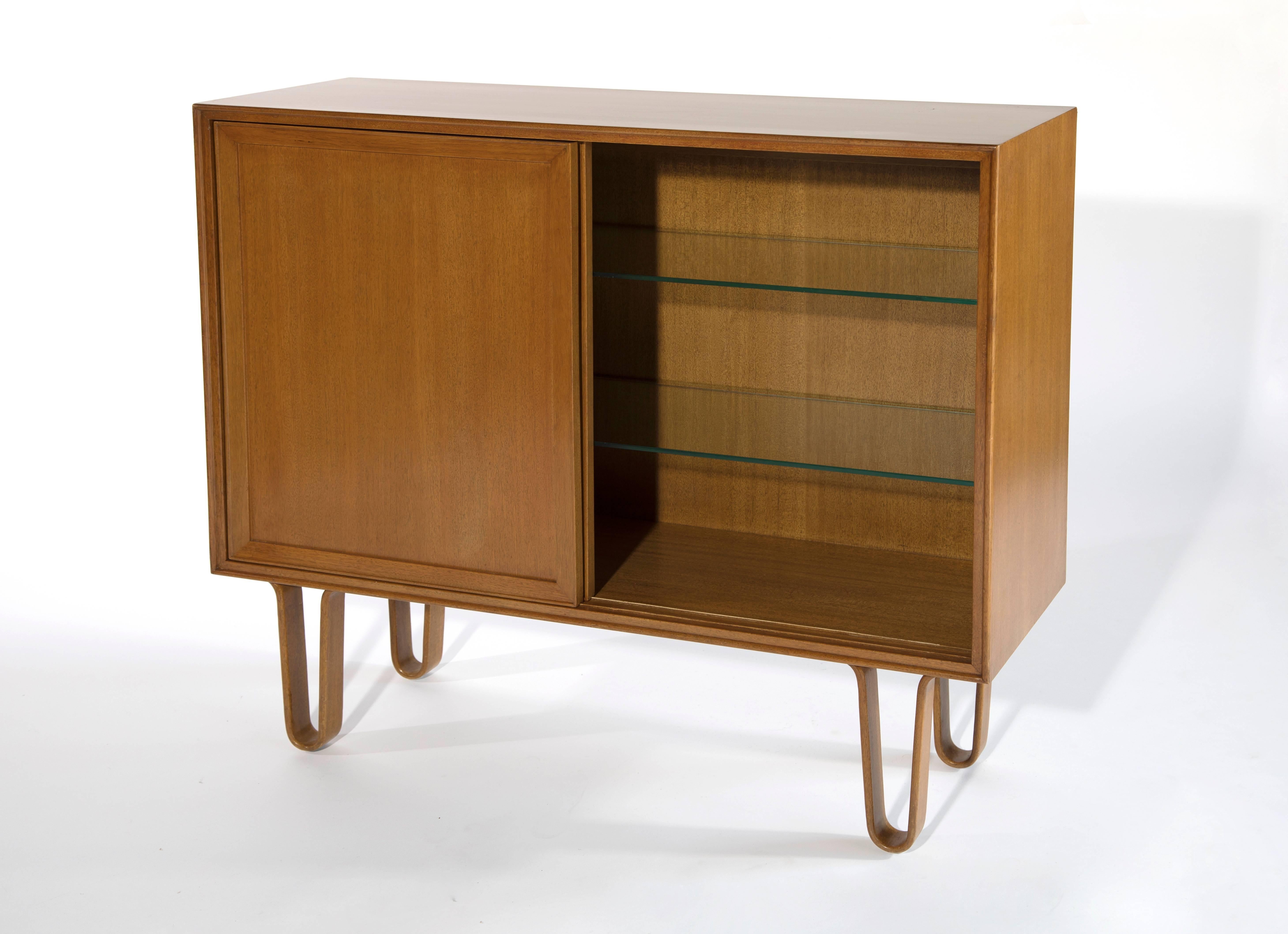 Sliding door bar cabinet on hairpin legs by Edward Wormley for Dunbar, model 4604.

USA, circa 1940s-1950s.

Laminated bentwood loop legs with two adjustable interior glass shelves.

Bleached mahogany or glass.
Measures: 36.26 H x 40.125 W x