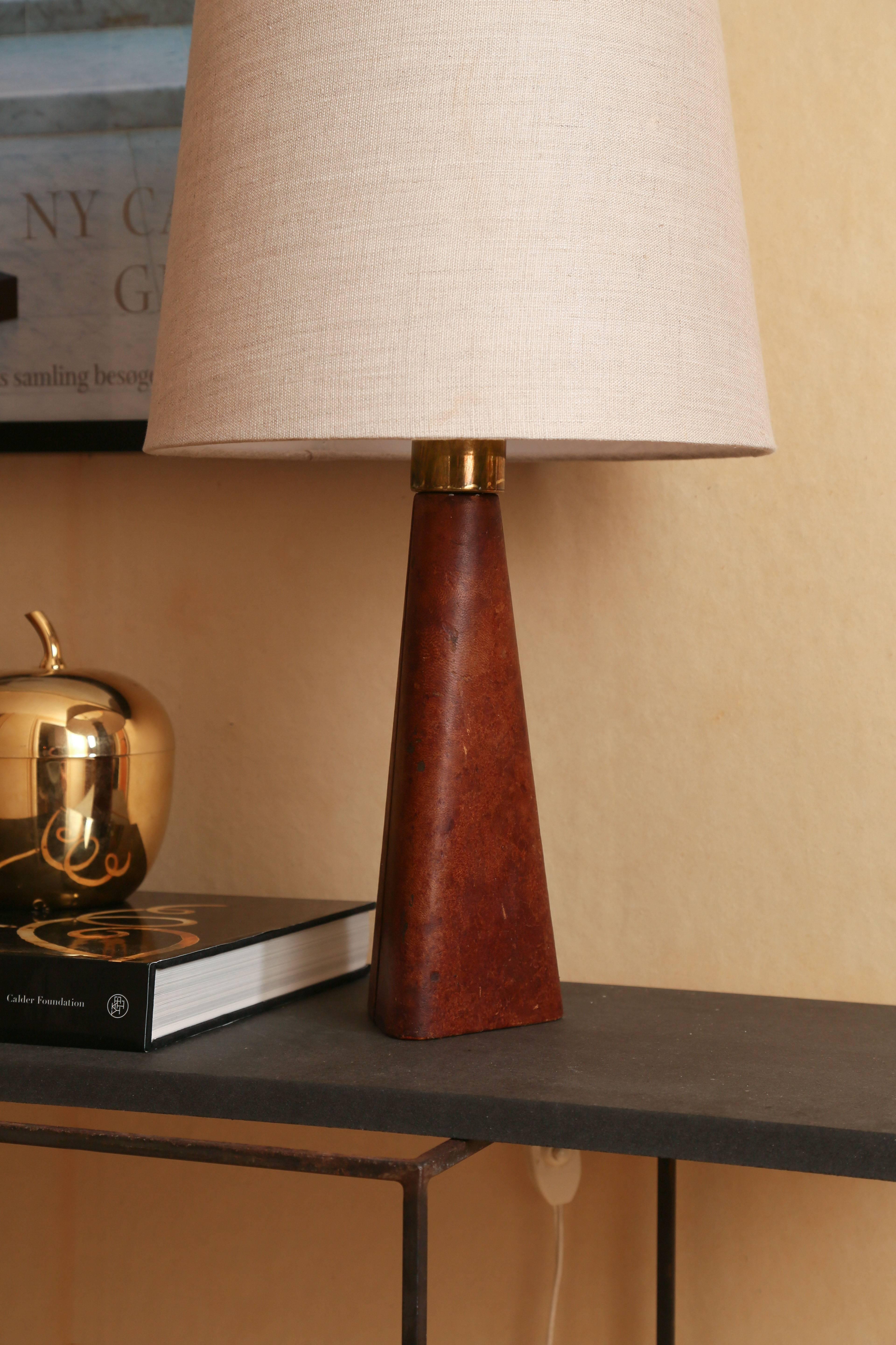 Triangle shaped table lamp by Lisa Johansson-Pape, model No.46-186.

Manufactured by Stockmann-Orno Oy

Finland, circa 1950s

Brown leather covered base with brass fittings.

Manufacturer's mark ST underside

Newly upholstered linen shade.