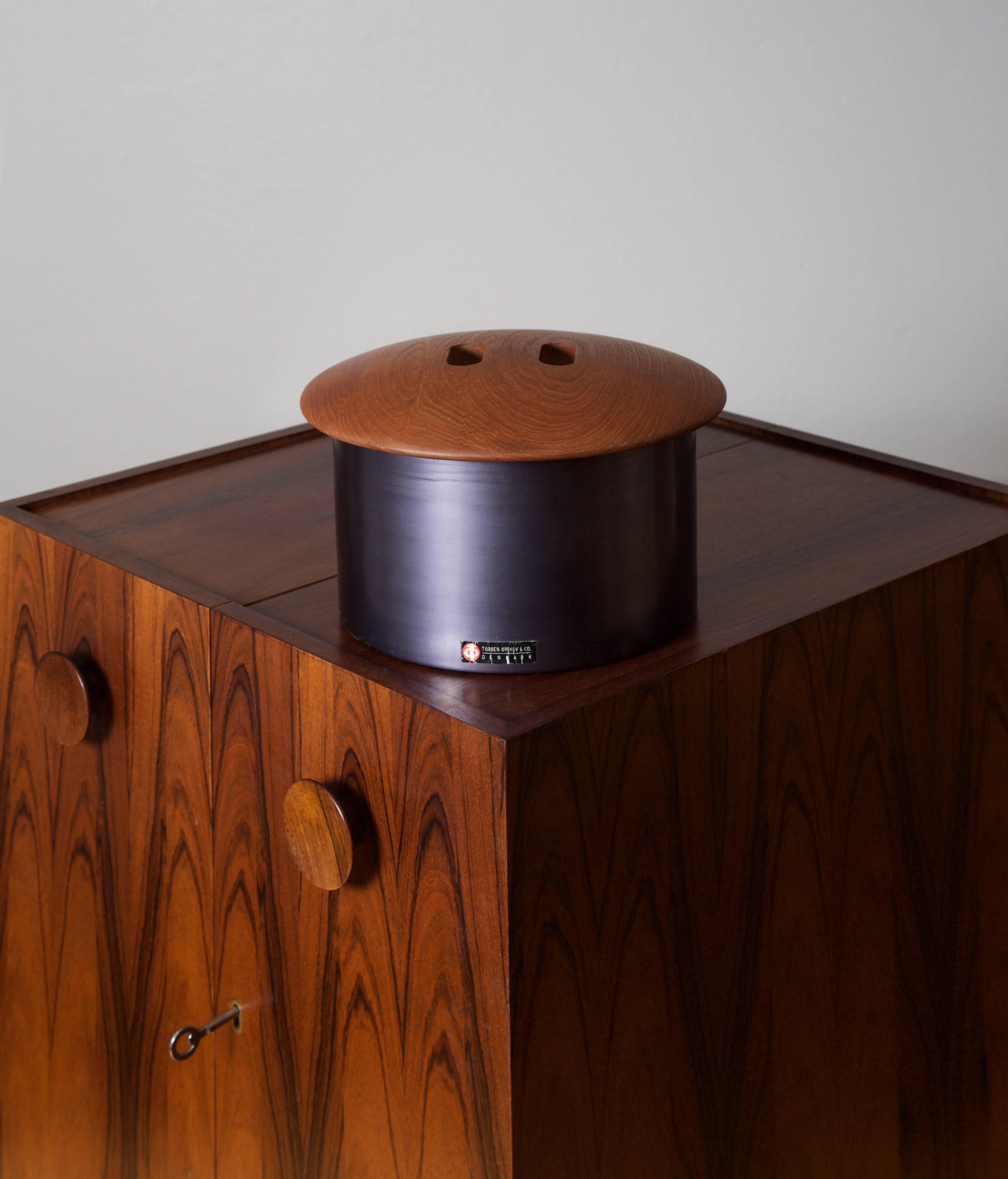 A rare ice bucket by Finn Juhl, manufactured by Torben Orskov & Co, Denmark. 

Material anodized aluminum with solid teak cover, red plastic interior,
Denmark, circa 1958.

Measurements: Diameter 25 cm, height 16 cm.

The model was first presented