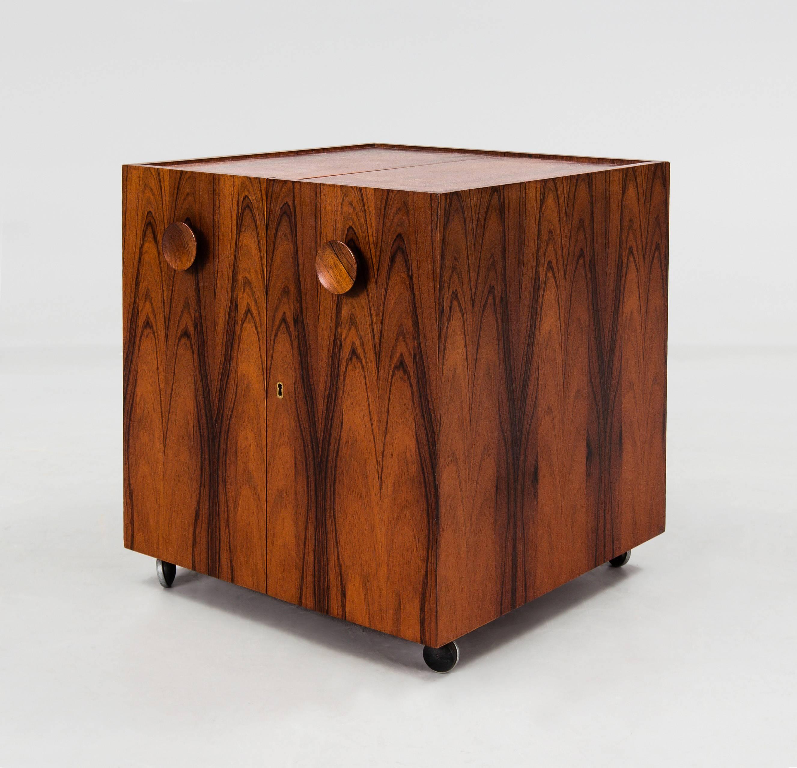 Square bar cabinet designed by Erik Buch, manufactured by Dyrlund

Denmark, circa 1960s

Rosewood with brass details, two adjustable/removable linoleum trays and six metal wheels under. 

The cabinet could be locked, original key