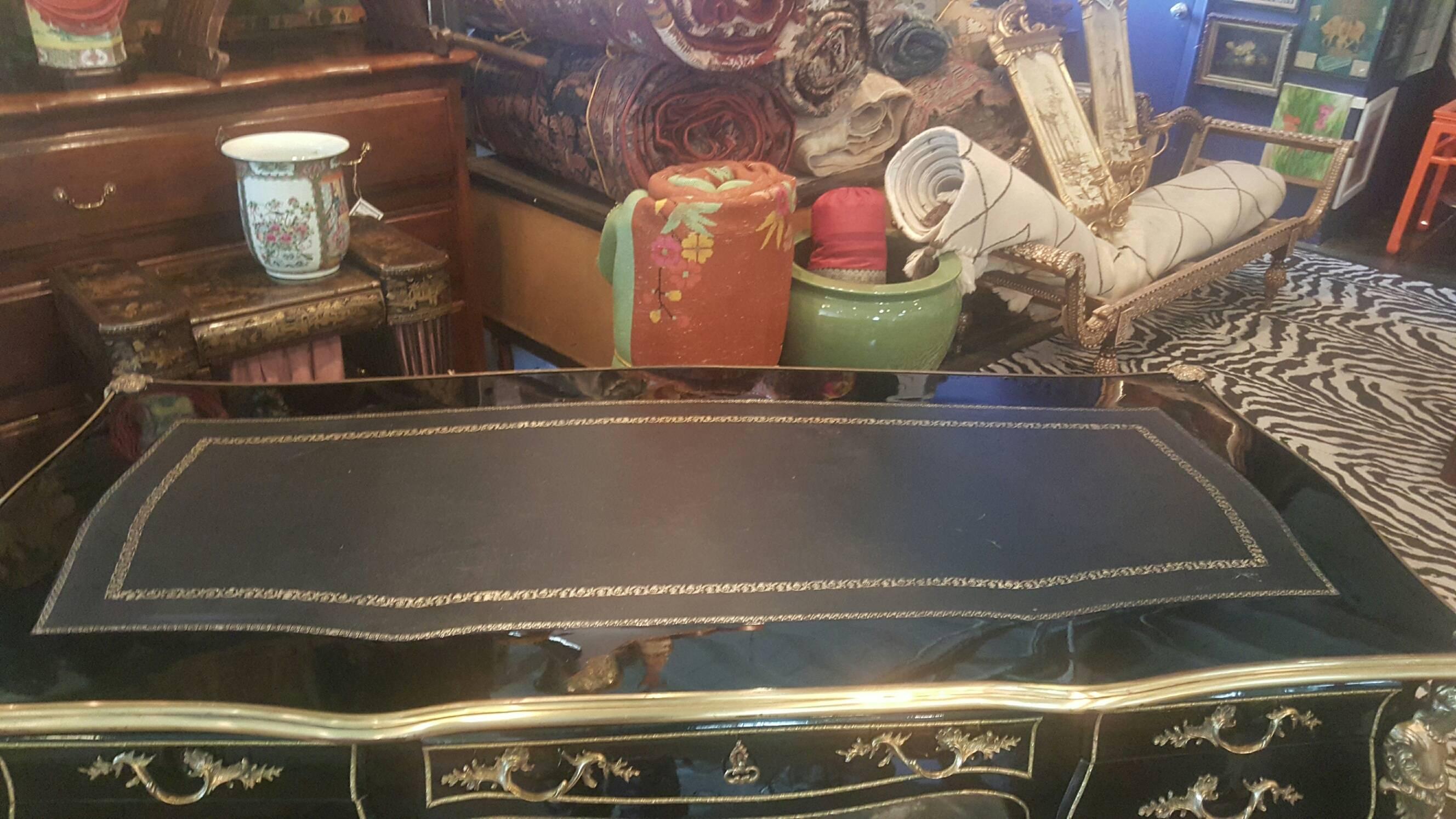 Vintage black lacquer bureau plat writing desk. Gilt bronze details. Elaborate figures on four corners. Gold tooled black leather top. Faux drawers on guest side of desk.