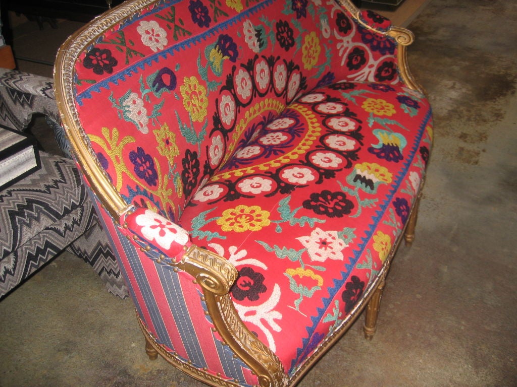 Carved and giltwood settee in vintage Suzani upholstery. Back is upholstered in a coordinating red and blue striped fabric. Brass nailhead trim.