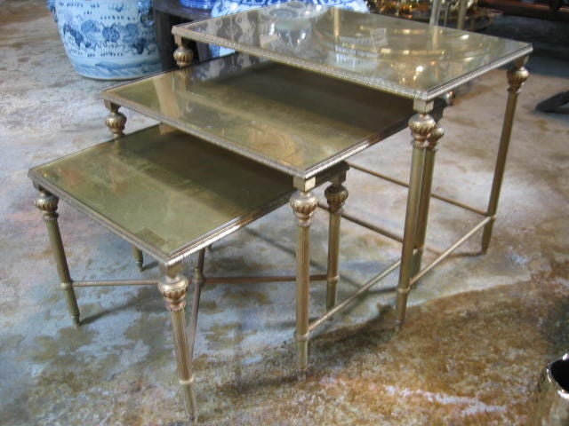 Nesting tables in Neoclassic style with gold-leafed mirrored tops. Antiqued finish with some distressing due to age. Bronze frames and legs have an antiqued patina.
