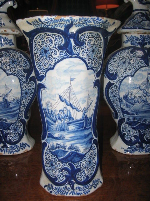 Hand-painted set of blue and white delft porcelain. Three covered vases and two trumpet vases. The lids depict perched birds. The vases depict fishermen in a sailing ship.