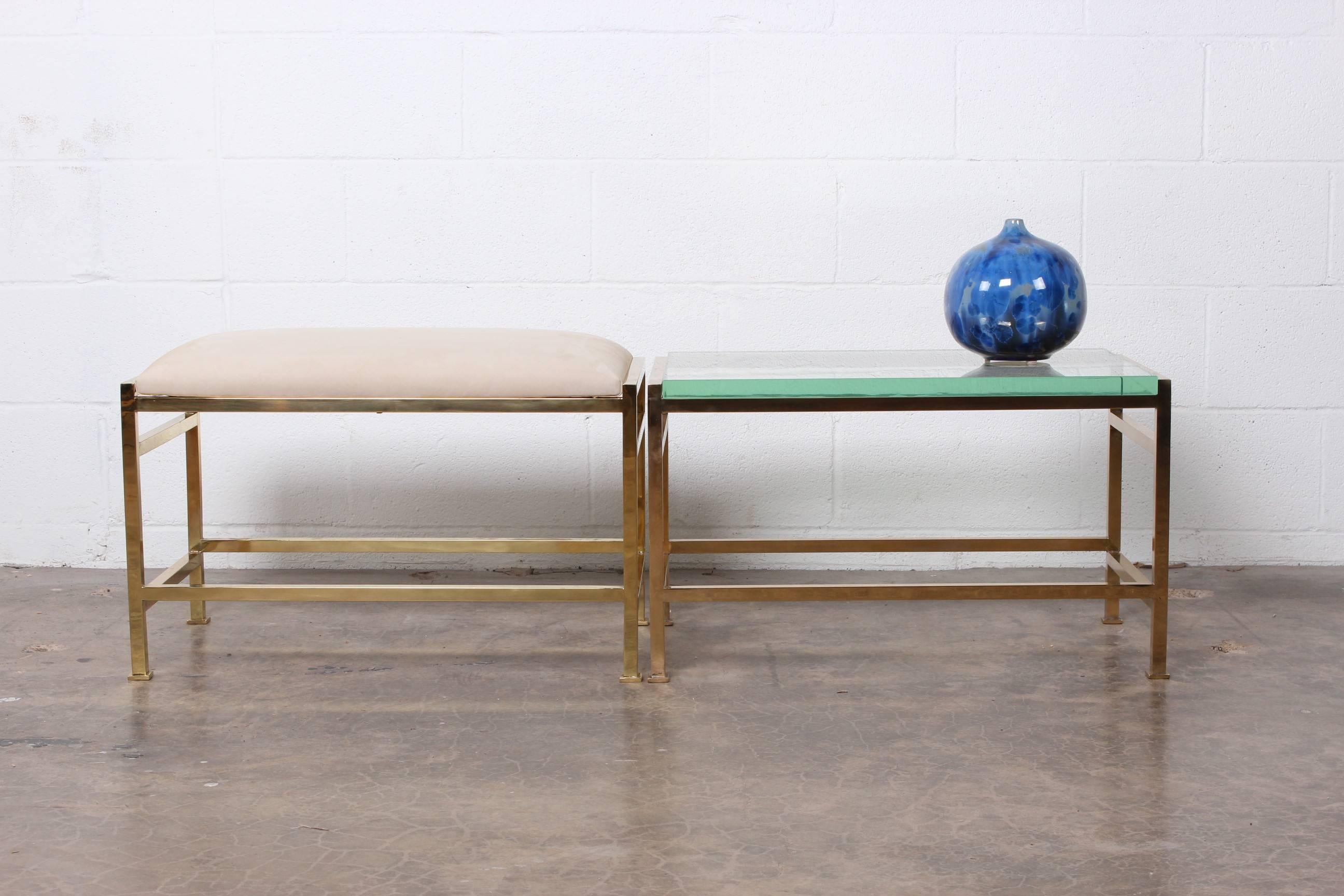 A brass bench with upholstered leather top and matching brass table with glass top. Designed by Edward Wormley for Dunbar. Priced and sold separately.