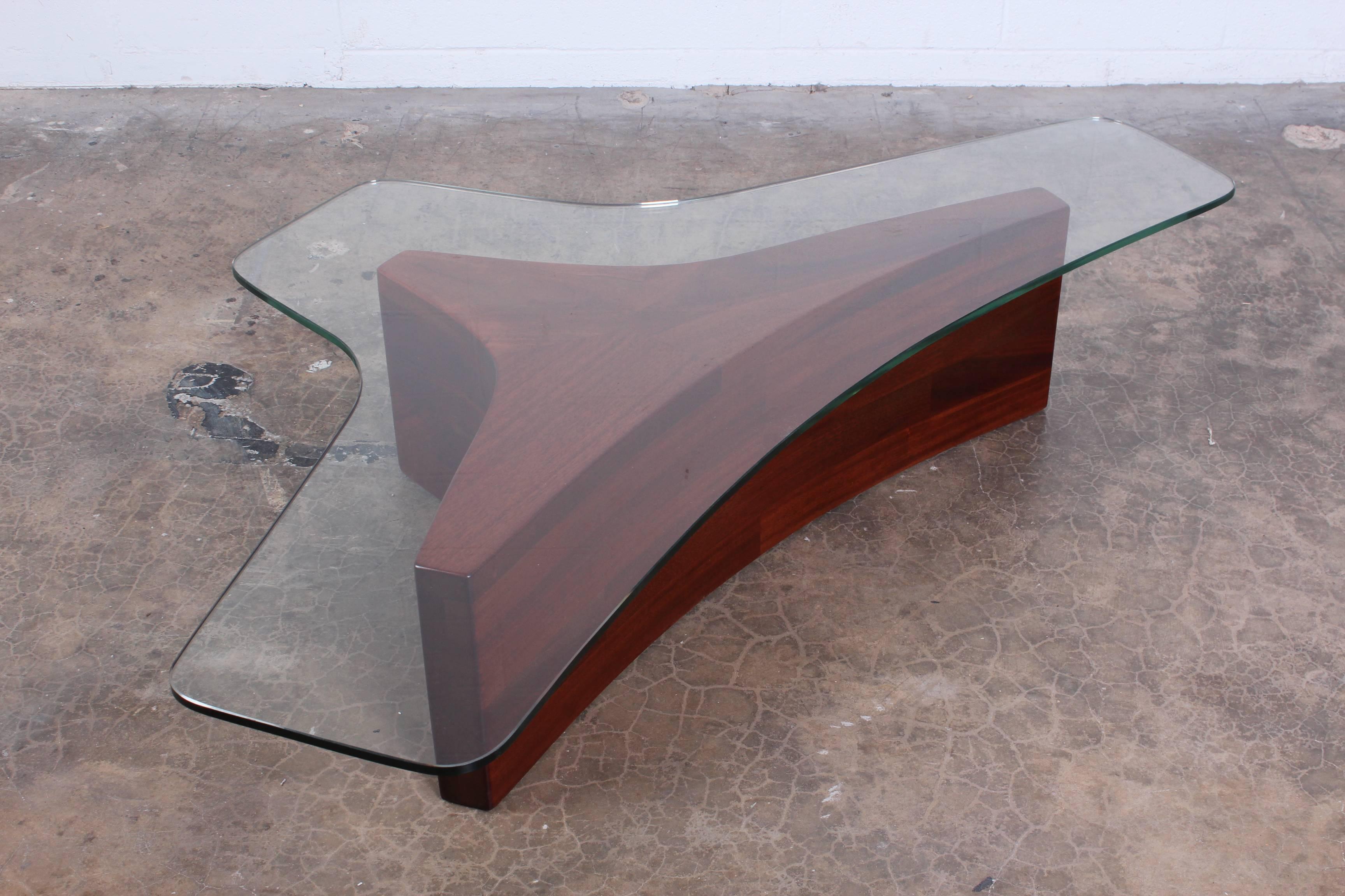 A sculptural mahogany coffee table with glass top. Designed by Vladimir Kagan.