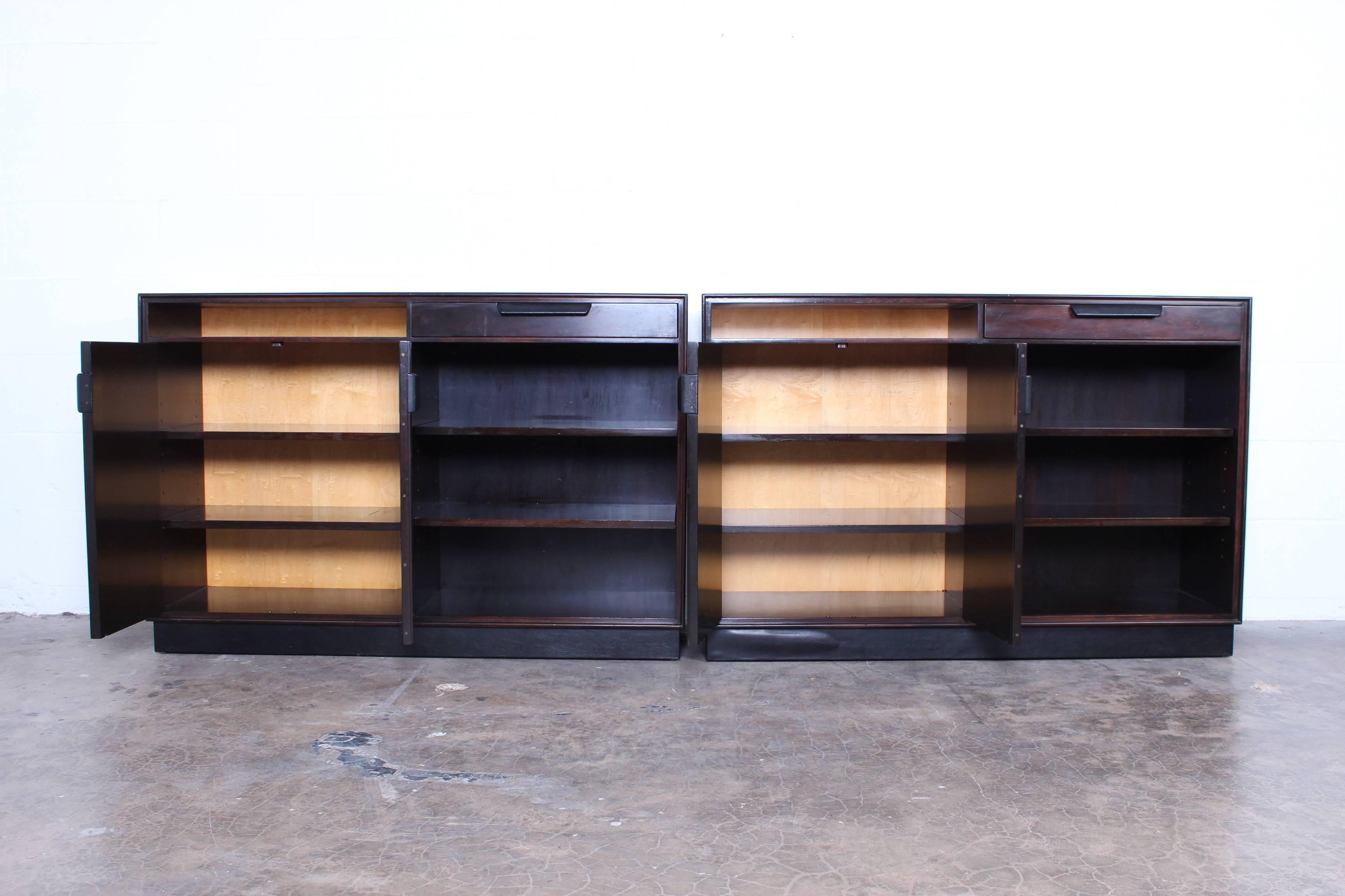 A pair of mahogany and maple cabinets with leather handles and adjustable shelves. Designed by Edward Wormley for Dunbar.