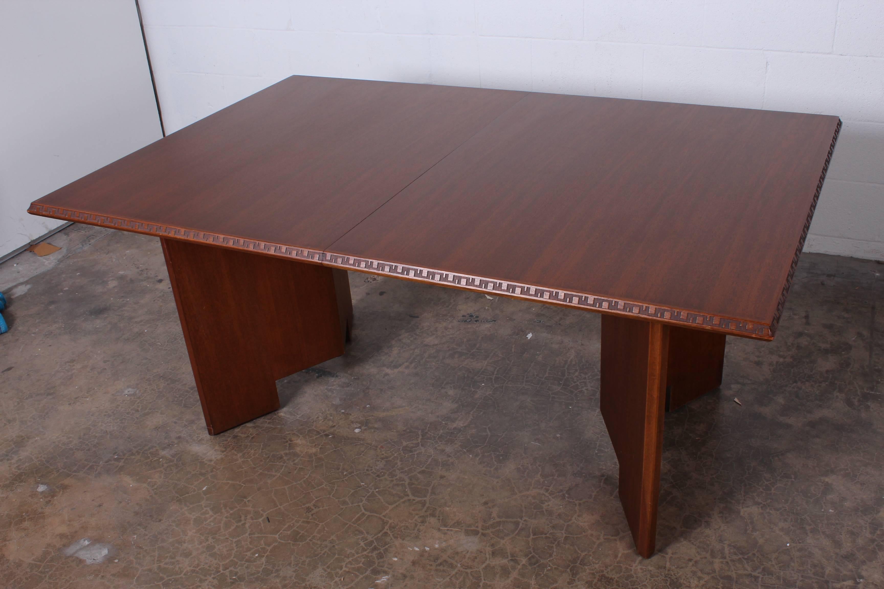 A mahogany dining table with Greek key Taliesin detail. Designed by Frank Lloyd Wright for Henredon. Table measures 5'4 without leaves and comes with two 18
