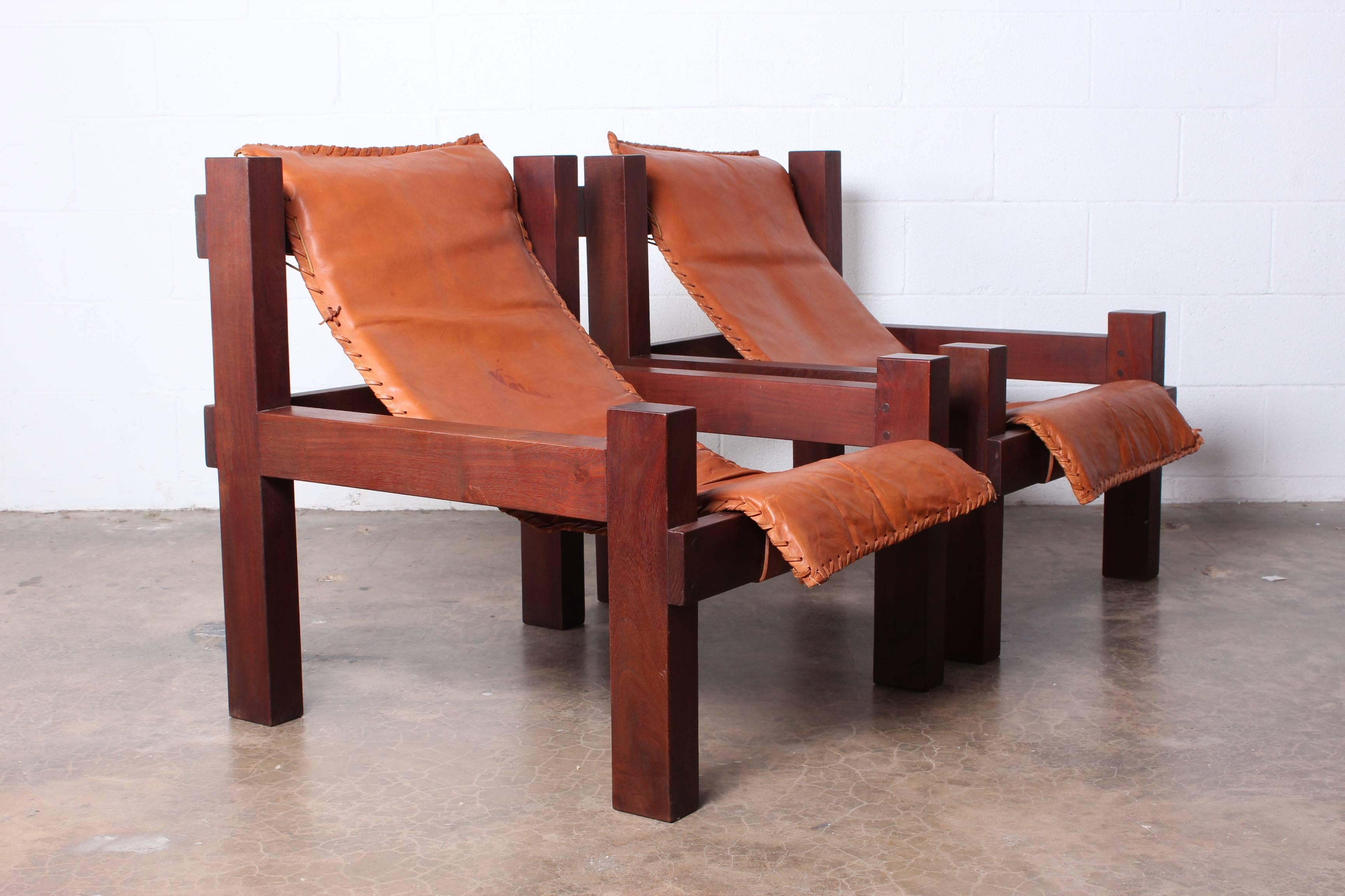 A pair of nicely scaled solid wood lounge chairs with patinated leather slings.