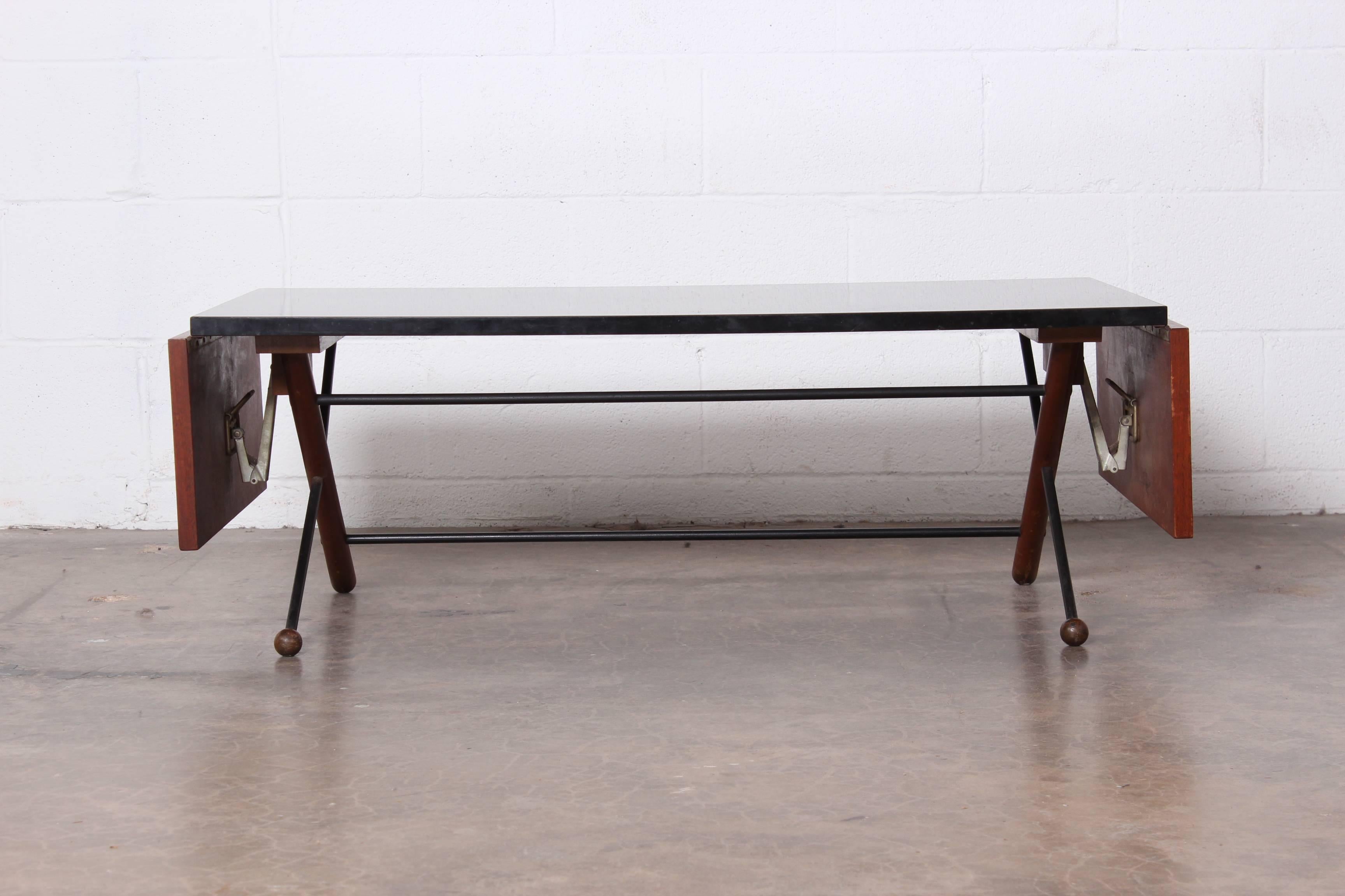 A rare drop-leaf coffee table designed by Greta Magnusson Grossman. Laminate top with walnut leaves and iron base. Table features two 8-inch drop-leaves; table measures forty-three inches when leaves are down.