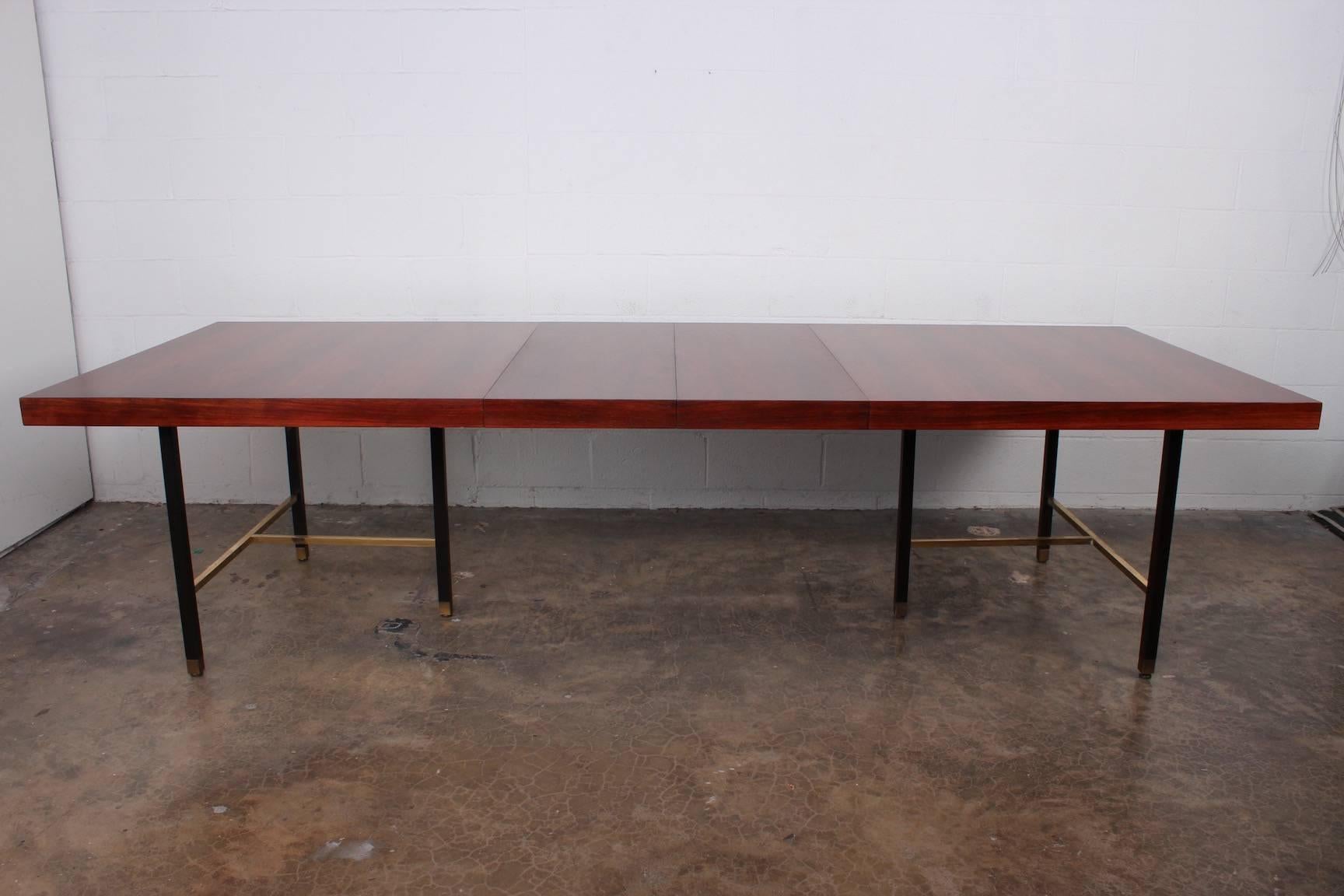 A large rosewood dining table on mahogany base with brass stretchers. Designed by Harvey Probber. Measures: 112