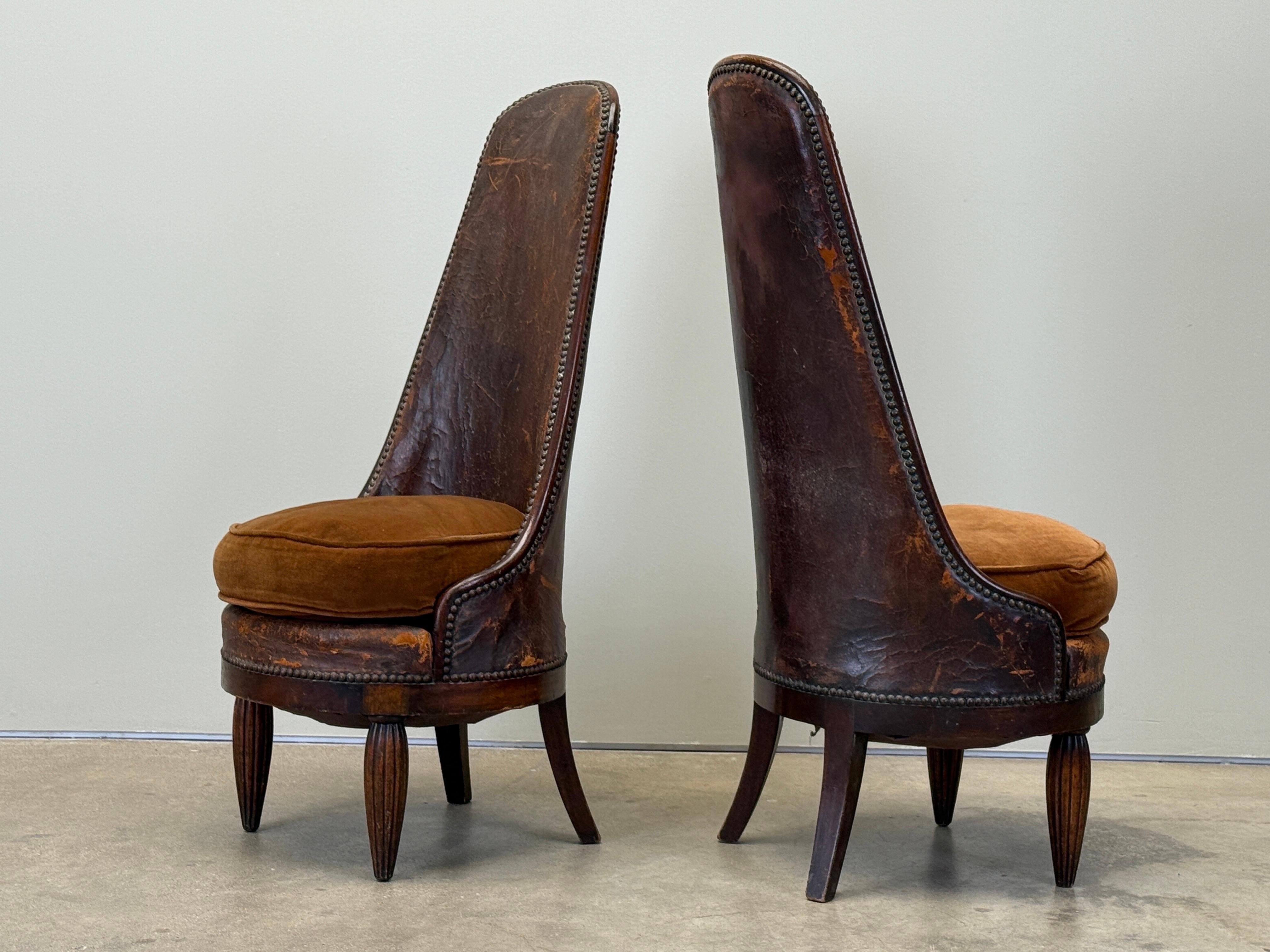 A pair of high back chairs with mahogany details by Maurice Dufrêne. Original wood finish shows wear and patina. The leather shows heavy wear with one chair having a large rip to the front and the other a large rip to the back (currently taped).