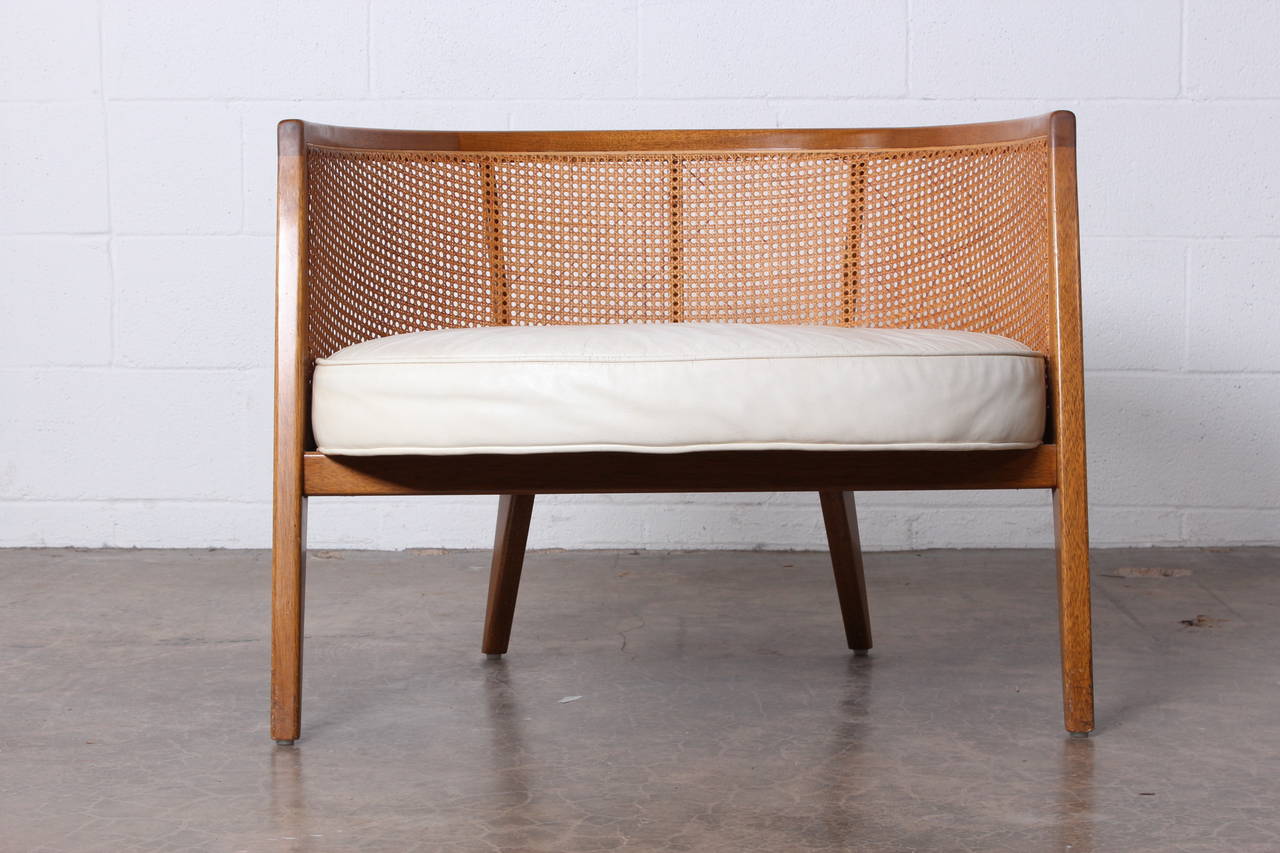 A mahogany and cane lounge chair with original white leather. Designed by Harvey Probber.