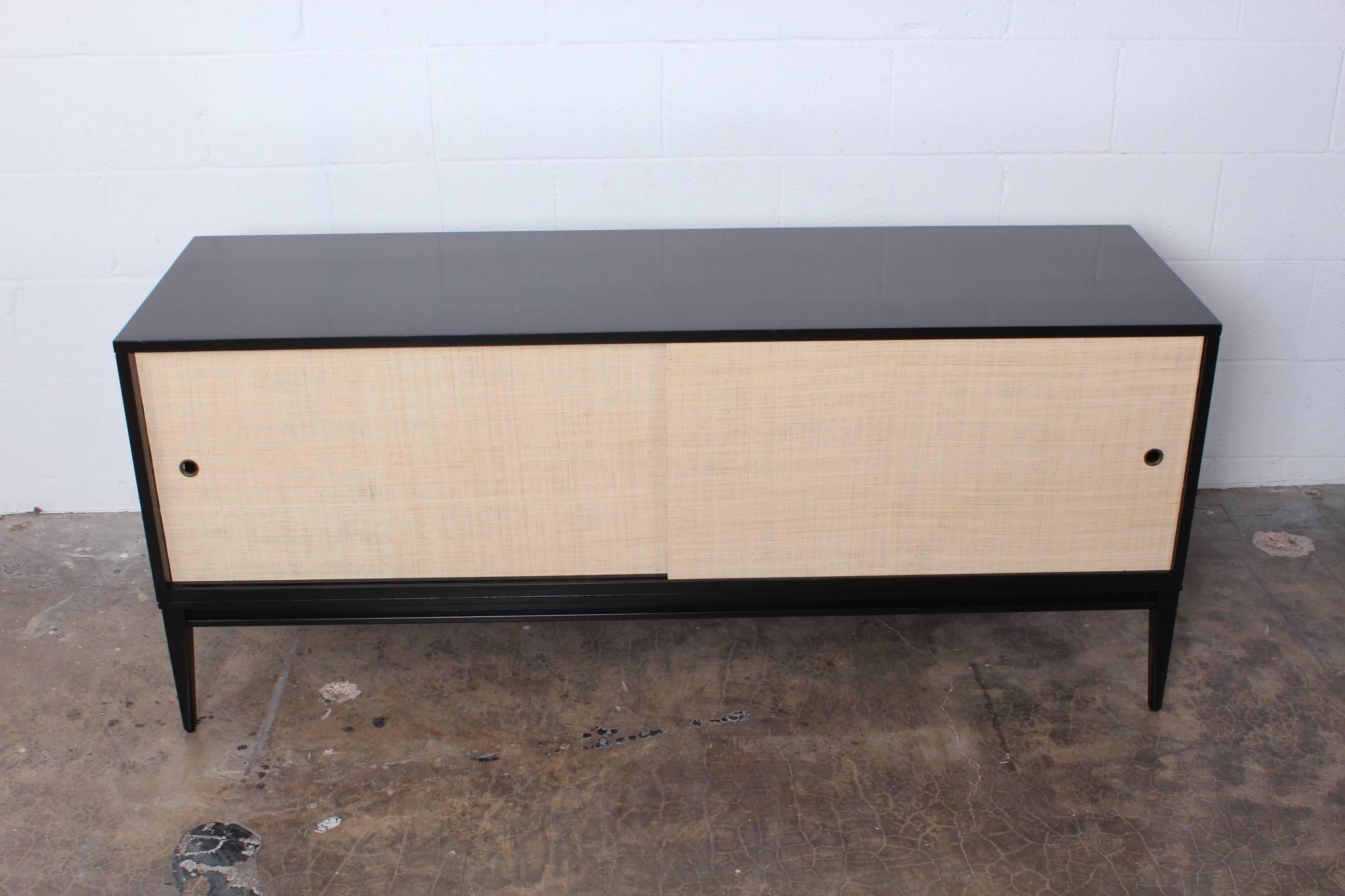 A black lacquered credenza with grasscloth doors and adjustable shelves. Designed by Paul McCobb for Winchendon.