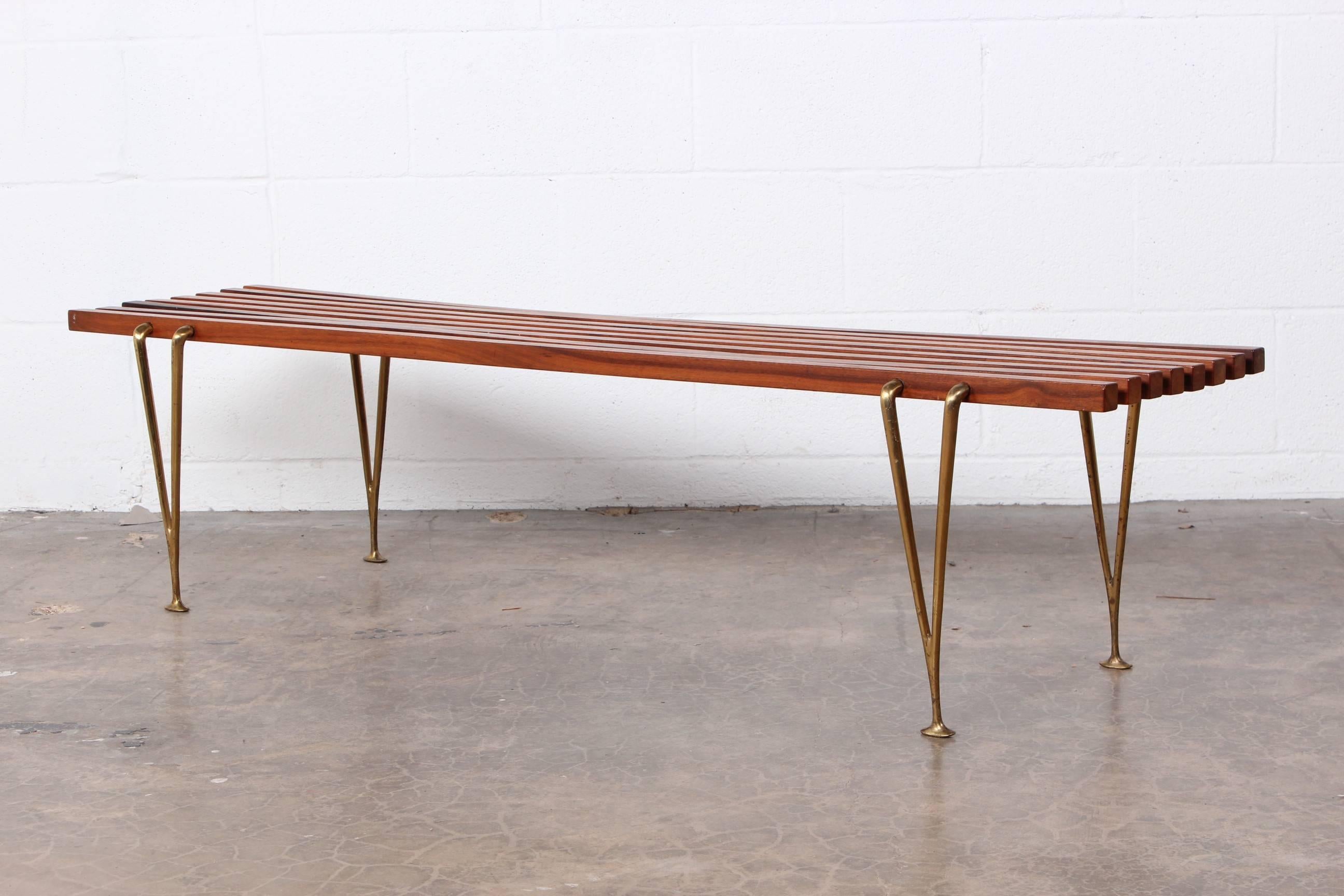 A walnut slat bench with brass legs designed by Hugh Acton.