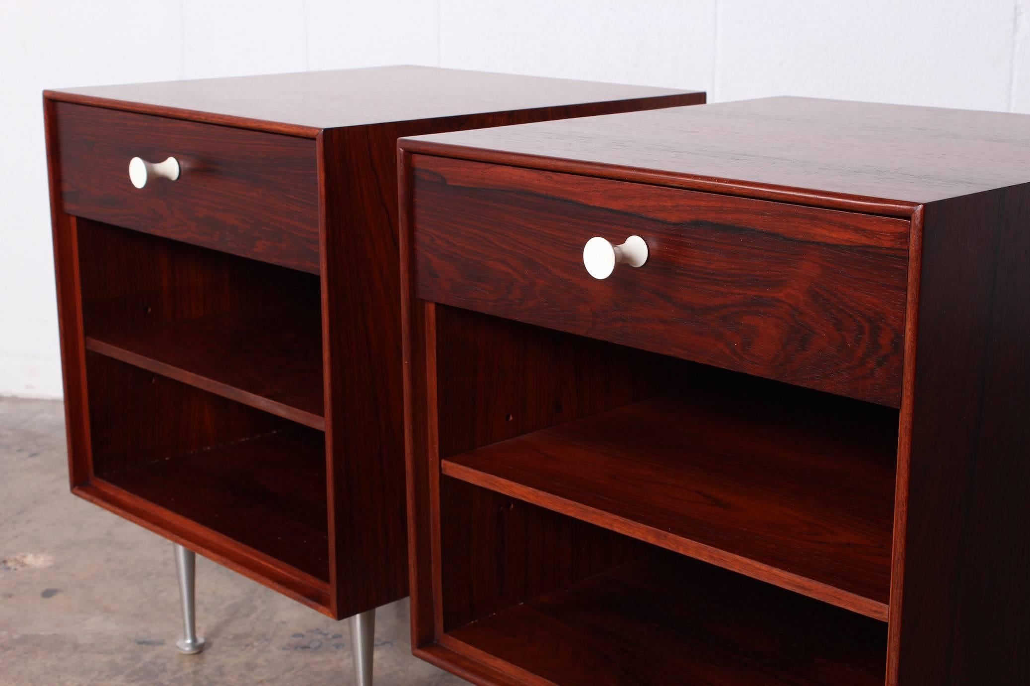 A pair of rosewood thin edge nightstands with aluminium legs and porcelain pulls. Each with adjustable rosewood shelf. Stamped 