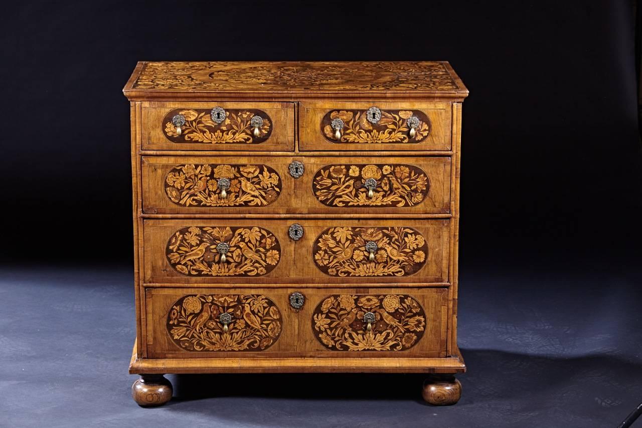 A walnut and marquetry chest of drawers with split upper drawers over three graduated long drawers and resting on ball feet. The elaborately inlaid panels on top, sides and front are decorated with complicated floral designs and with perched birds.