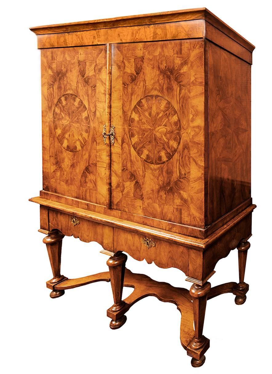 A fine example of a Dutch William and Mary two-door cabinet the top section having shelves, on a stand with two drawers and trumpet shaped legs, all veneered with choice burl walnut veneers.