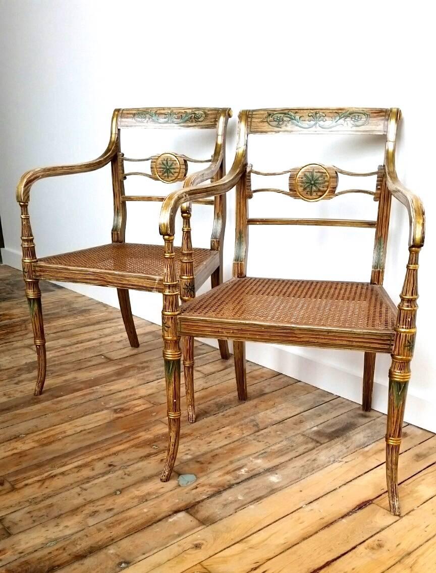 A fine pair of early 19th century elegant period Regency English armchairs with caned seats and silk cushions. The arms with striped parcel gilt decoration, the chairs overall with refreshed paint to simulate bamboo and stylized bamboo leaves, circa