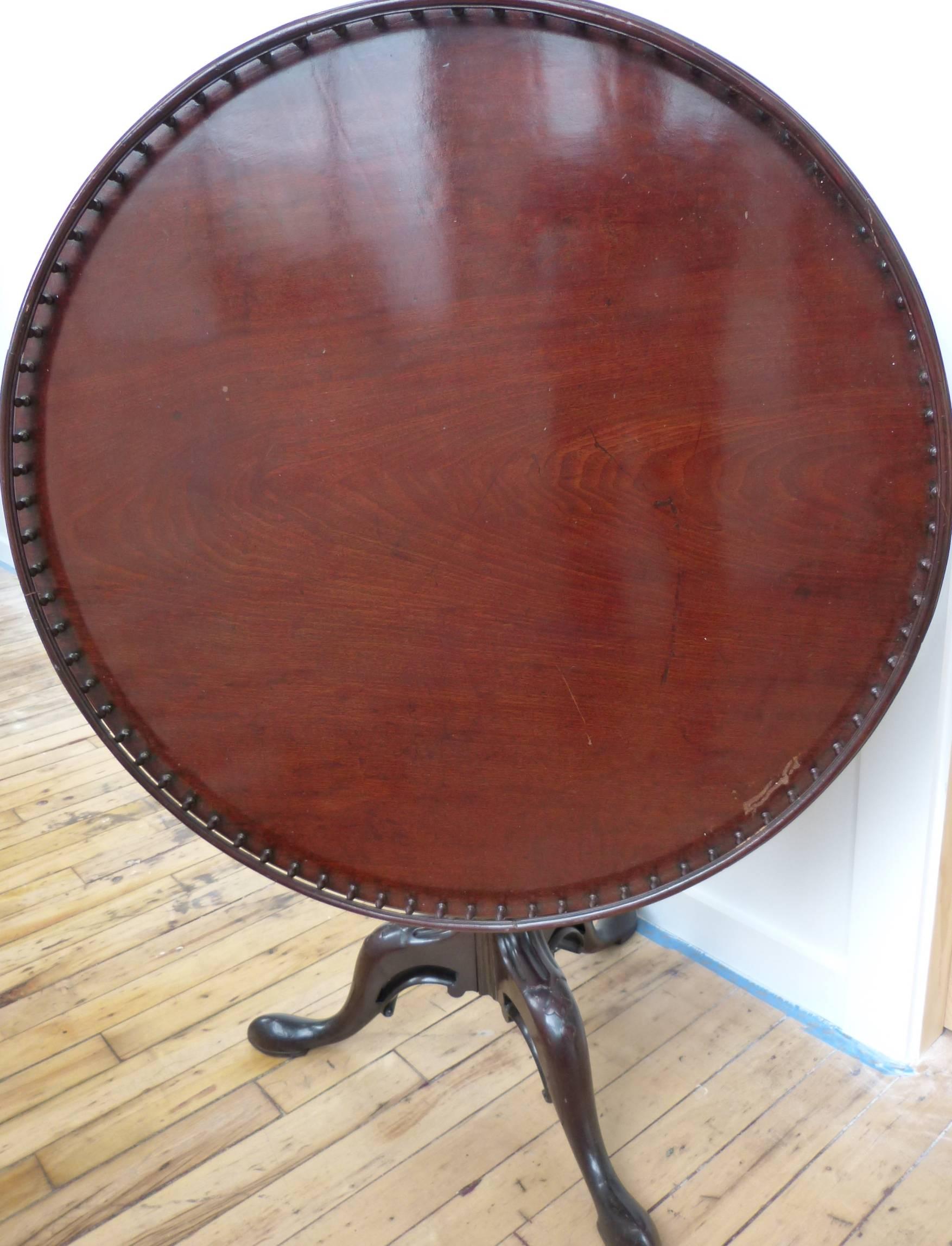A large fine quality Chippendale period mahogany tilt-top table on three shaped and carved with bellflower legs, ending in pad feet. The top is a 36-inch single plank of finely figured mahogany, the richly figured tilt-top with a shaped pierced