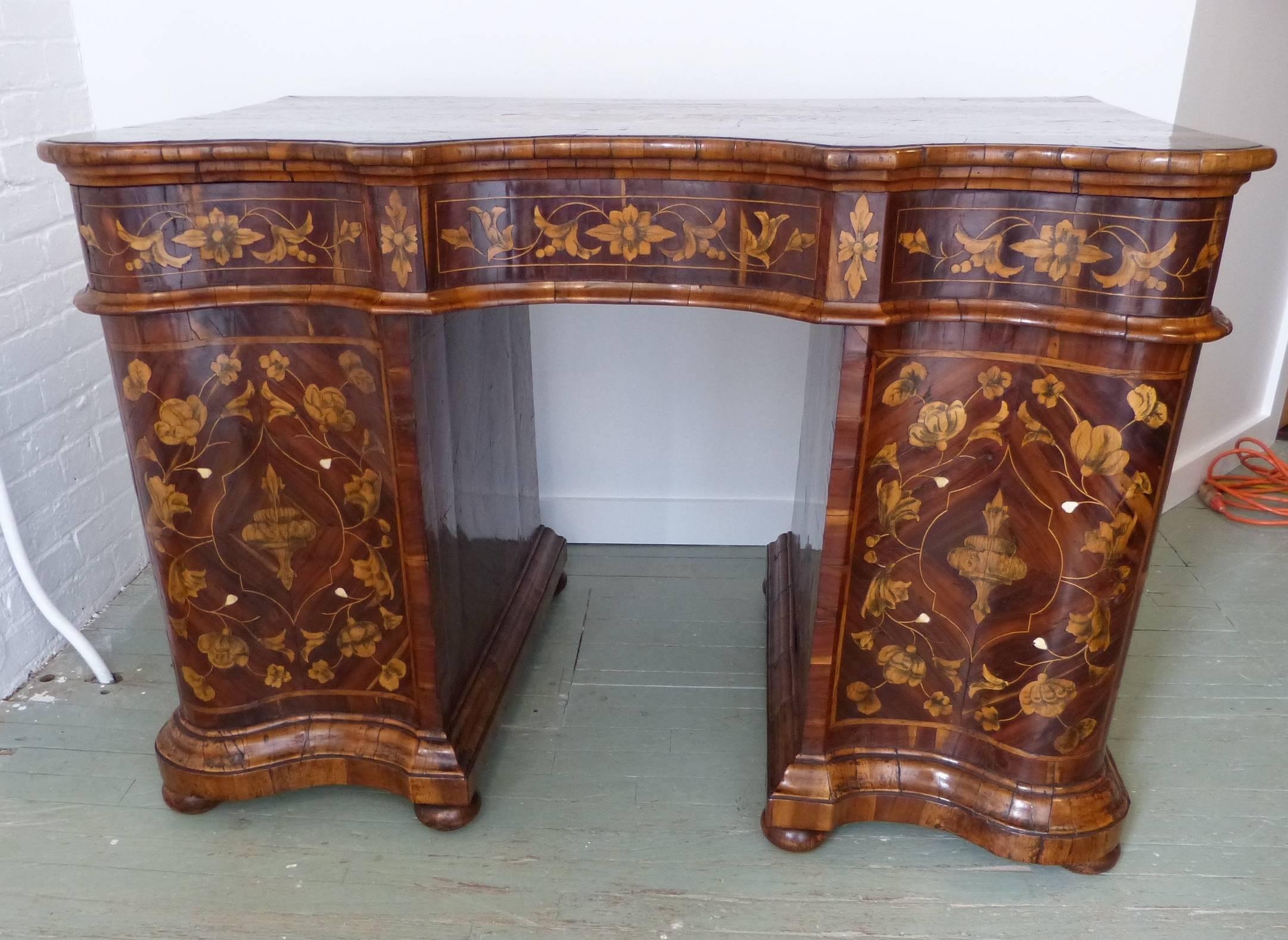 An exceptional 18th century inlaid desk, the front with a writing slide above two drawers and two cupboard doors, the back with exaggerated serpentine pedestals. Inlaid overall with shaped vines ending in simulated floral decoration, the top inlaid