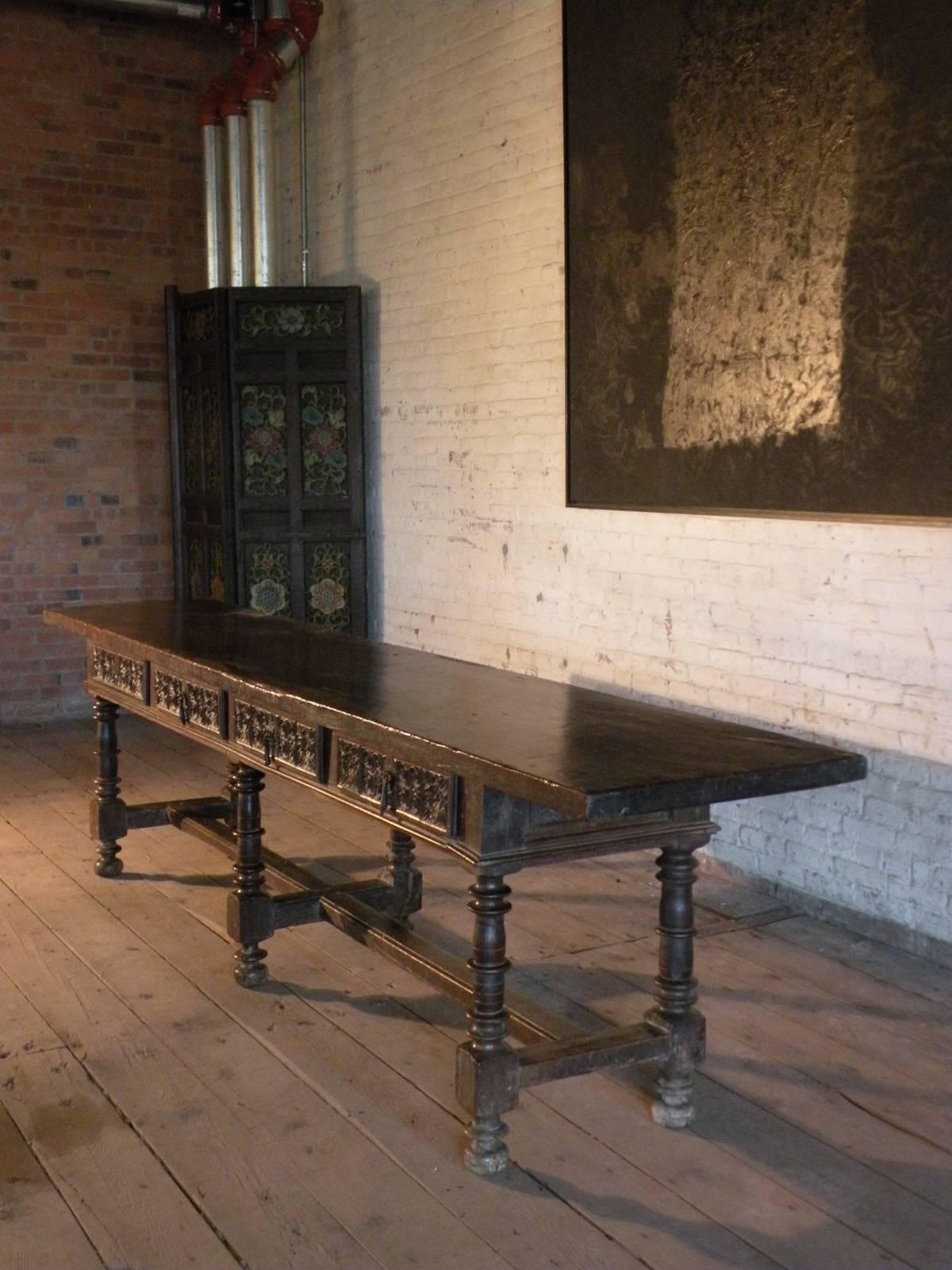 Extraordinary long and narrow walnut table, with a massive one-plank top, over a frieze containing four drawers with typical wrought iron pulls, conforming carved decoration on all four sides, the six symmetrically turned legs ending in bun feet and