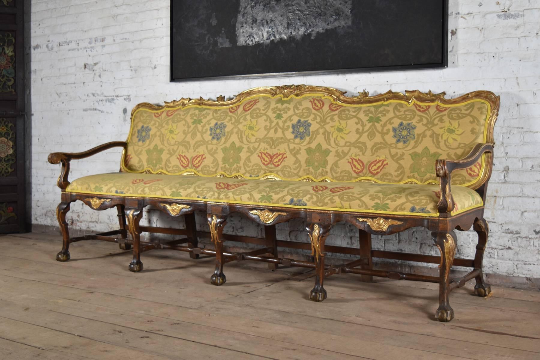 Exceptional, long open arm walnut sofa with carved and gilt accents, the cabriole legs ending in ball and claw feet and joined by stretchers.
