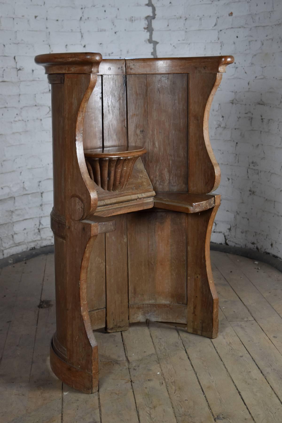 Tall, unusual and conceptual chair of half-round paneled form, The seat can be lifted on hinges forming a misericord supported by a fluted console.  A a rare and  form of free-standing choir stall, made of oak and having a beautiful unstained light