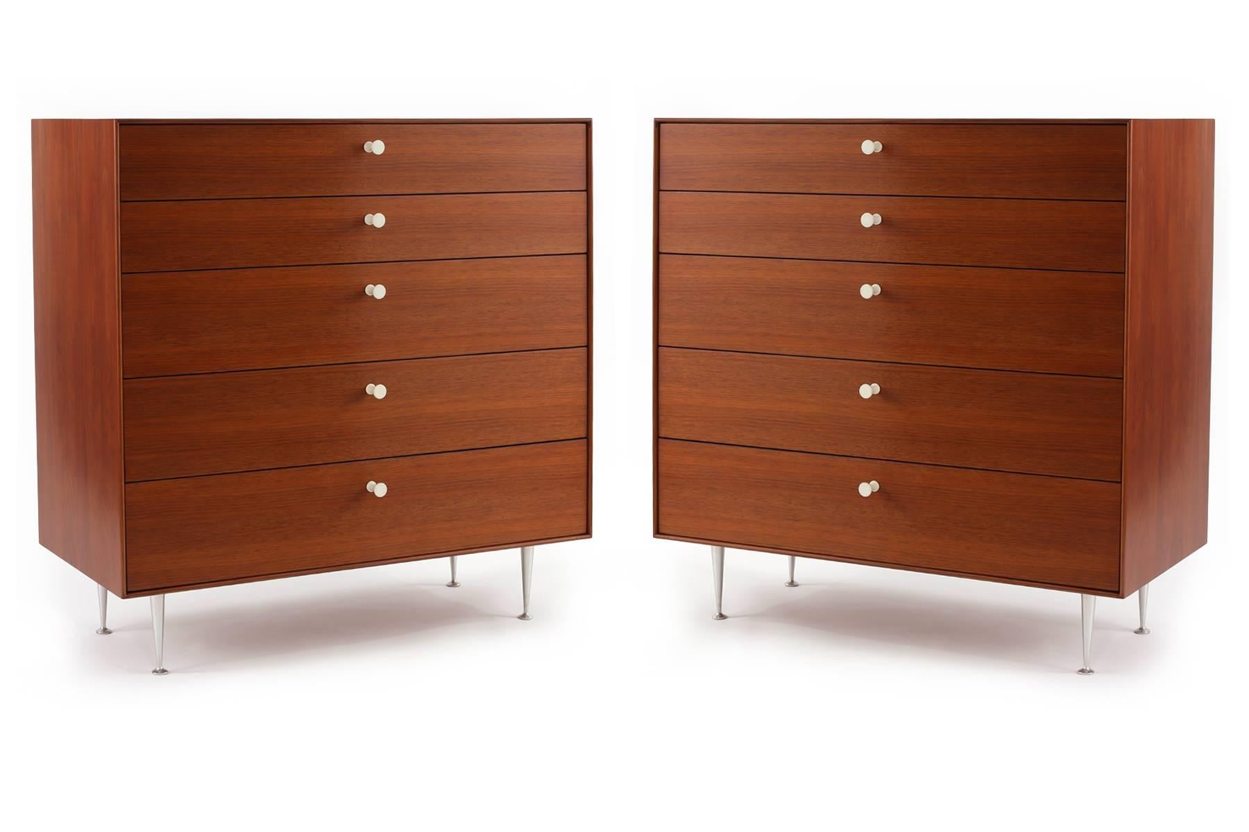 Early all original pair of George Nelson for Herman Miller thin edge chests of drawers, circa late 1950s. These five-drawer examples have combed walnut cases and drawer fronts with hourglass porcelain pulls and iconic tapered steel legs. Newly