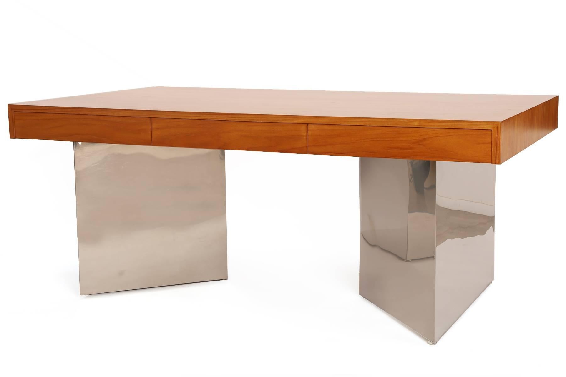 Teak and polished steel desk by Pace, circa early 1970s. This example has an exquisitely grained teak top with three inset drawers. Drawers have teak dividers within. The bases are triangular mirror polished steel over wood. The top of the desk has