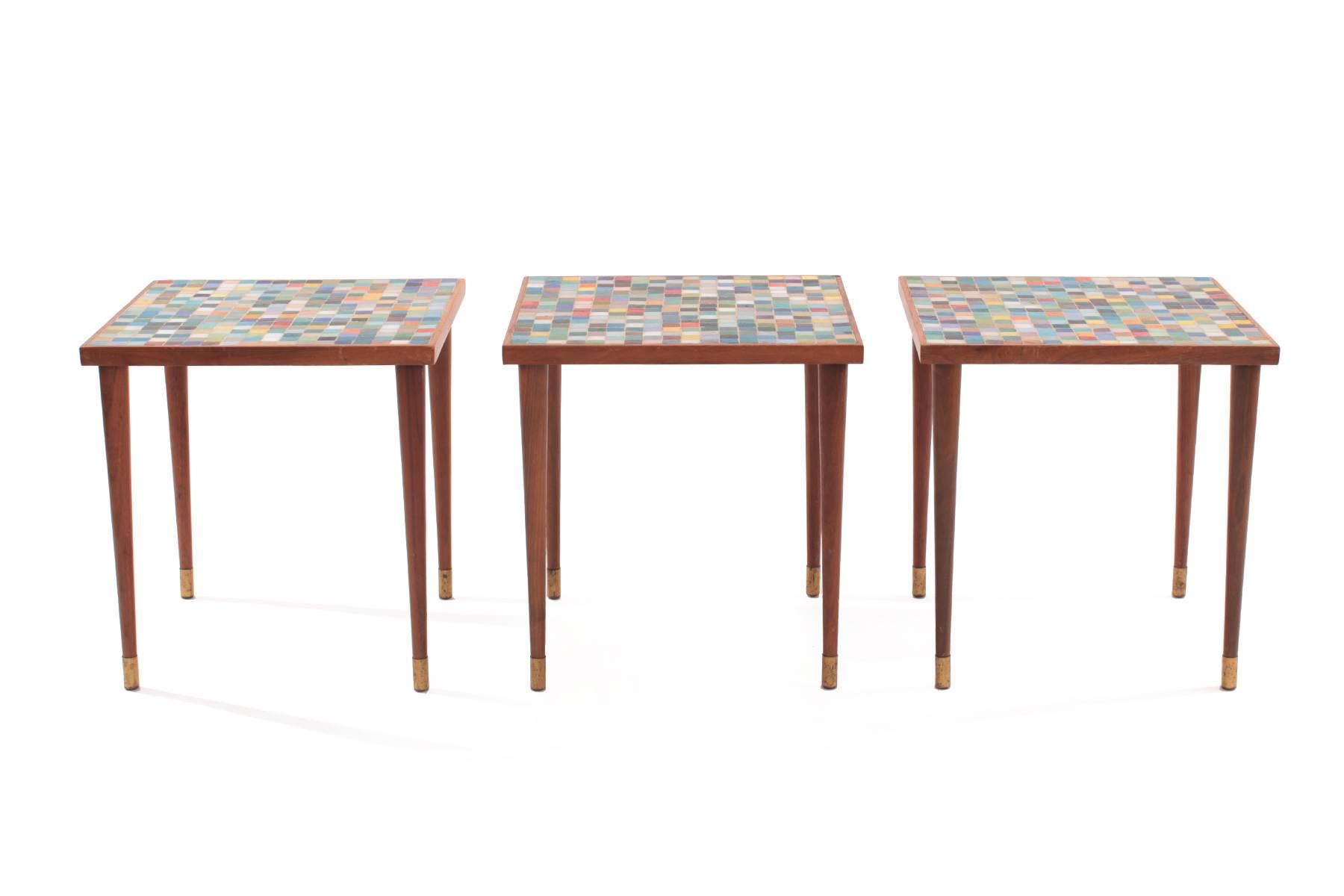 Three walnut brass and mosaic glass side tables circa late 1950s. These all original examples have tapered walnut legs with brass caps and lovely multi colored mosaic glass tops. Price listed is for the set of three.