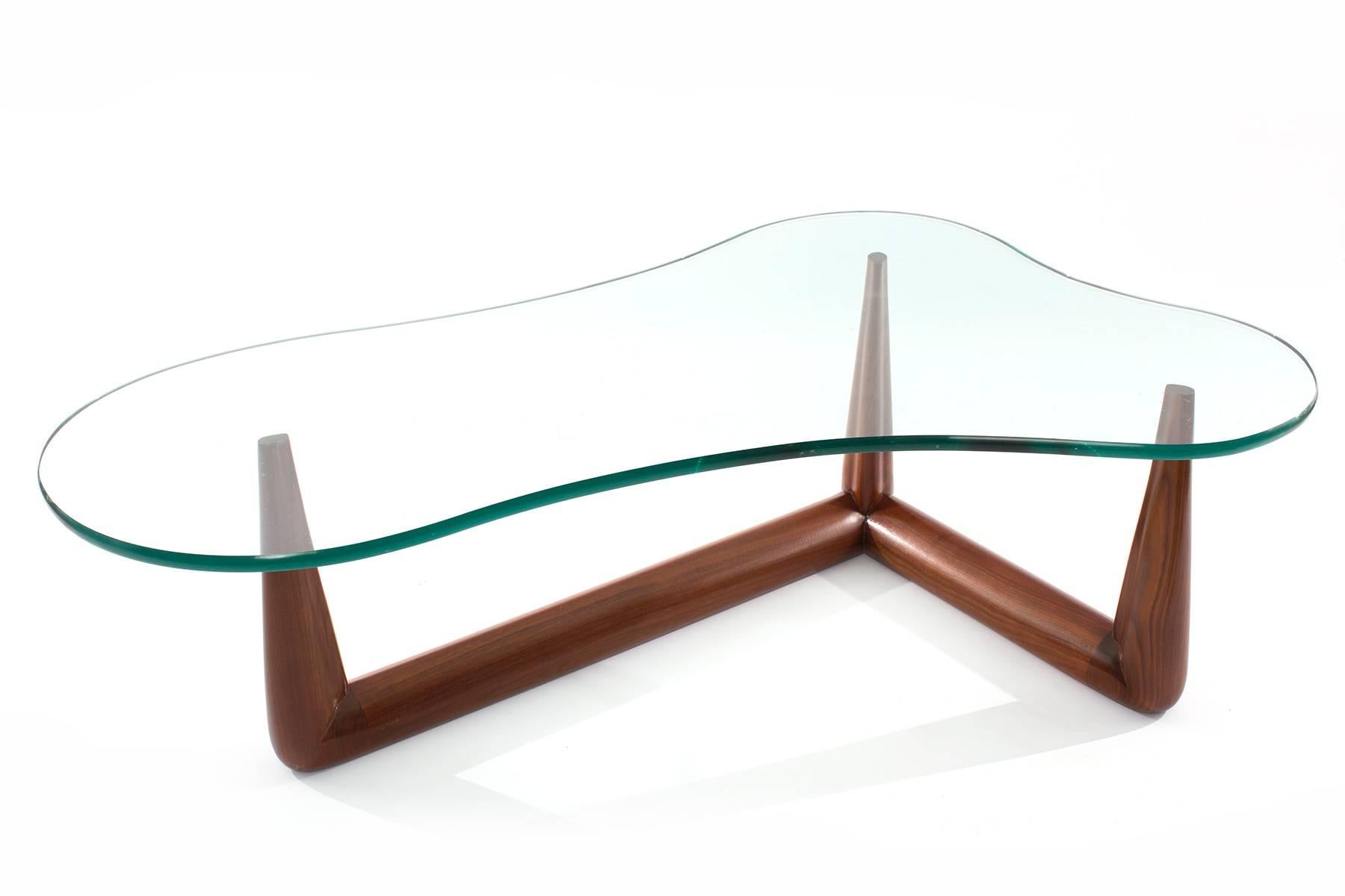 Free form glass and solid walnut cocktail table by T.H. Robsjohn Gibbings for Widdicomb circa early 1950s. 
This elegant example has a tapered solid walnut base that has been impeccably finished. The glass top is 0.75” thick.
