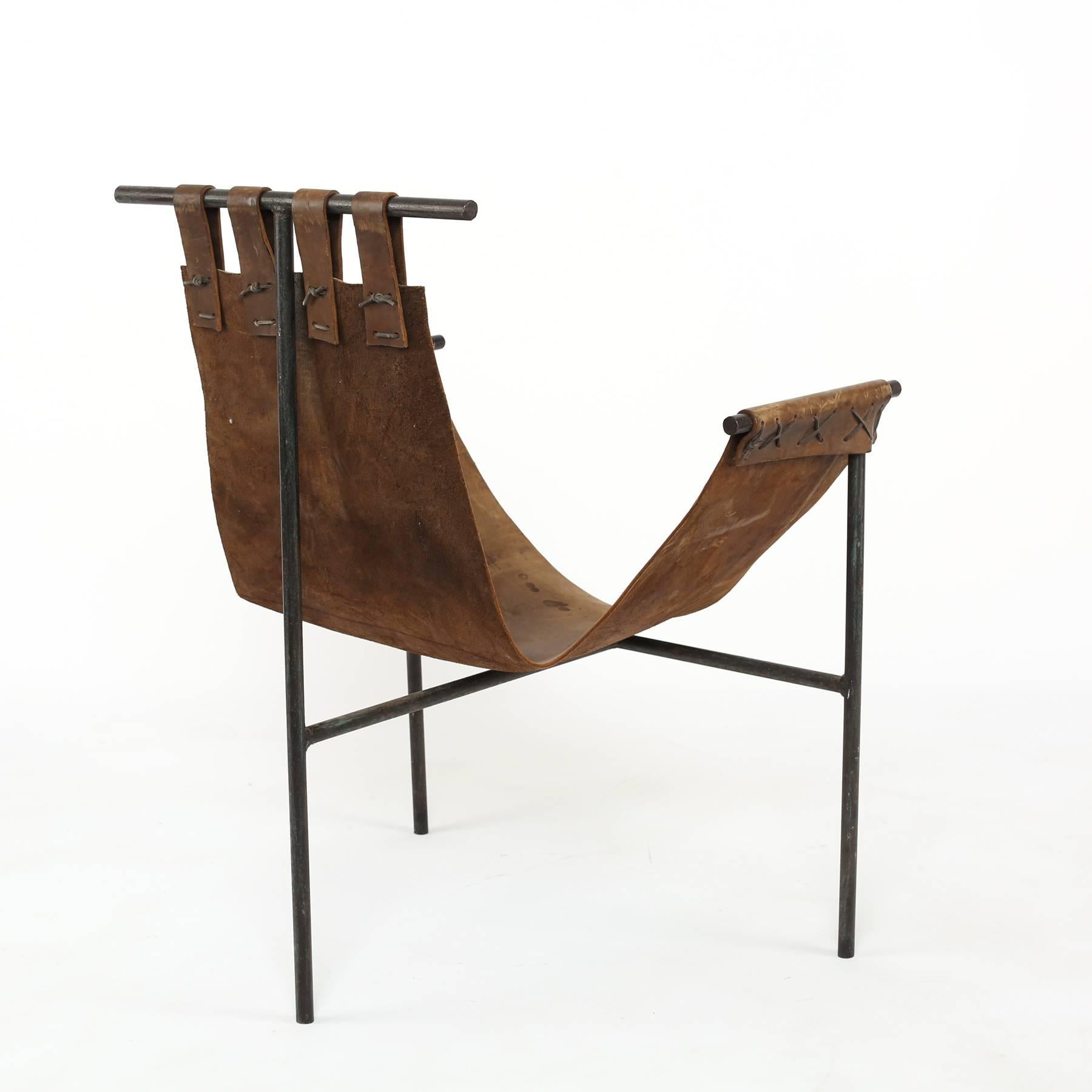 Iron and saddle leather sling chair, circa early 1970s. This example was designed by Bill Tull an Arizona architect. It has a beautifully patinated leather sling with a tripod leg iron frame.