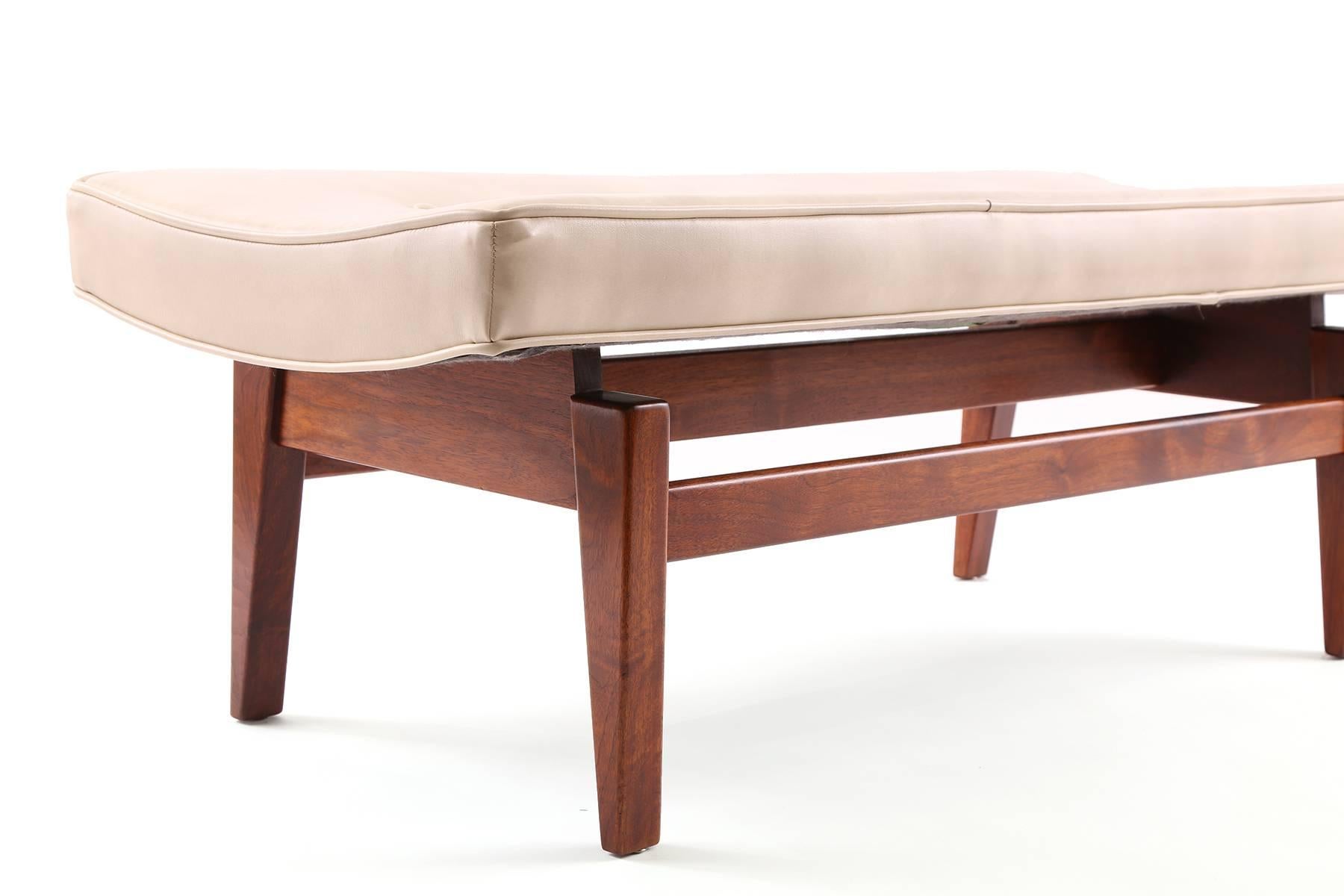 Jens Risom upholstered bench circa early 1960s. This all original example has a subtly curved cream vinyl top that sits atop a solid sculpted walnut base. 