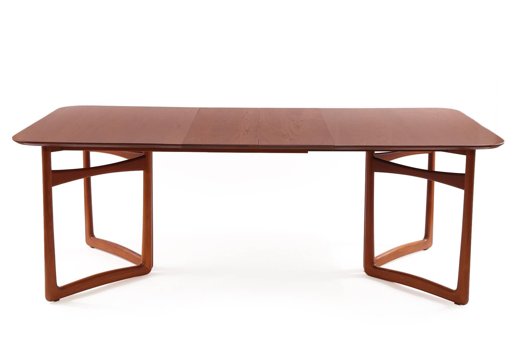 Solid teak and brass dining table by Peter Hvidt and Orla Molgaard Nielsen circa late 1950s. This all original example has sculptural solid teak legs and stretchers with patinated brass accents. It has a beautifully grained solid teak top with two
