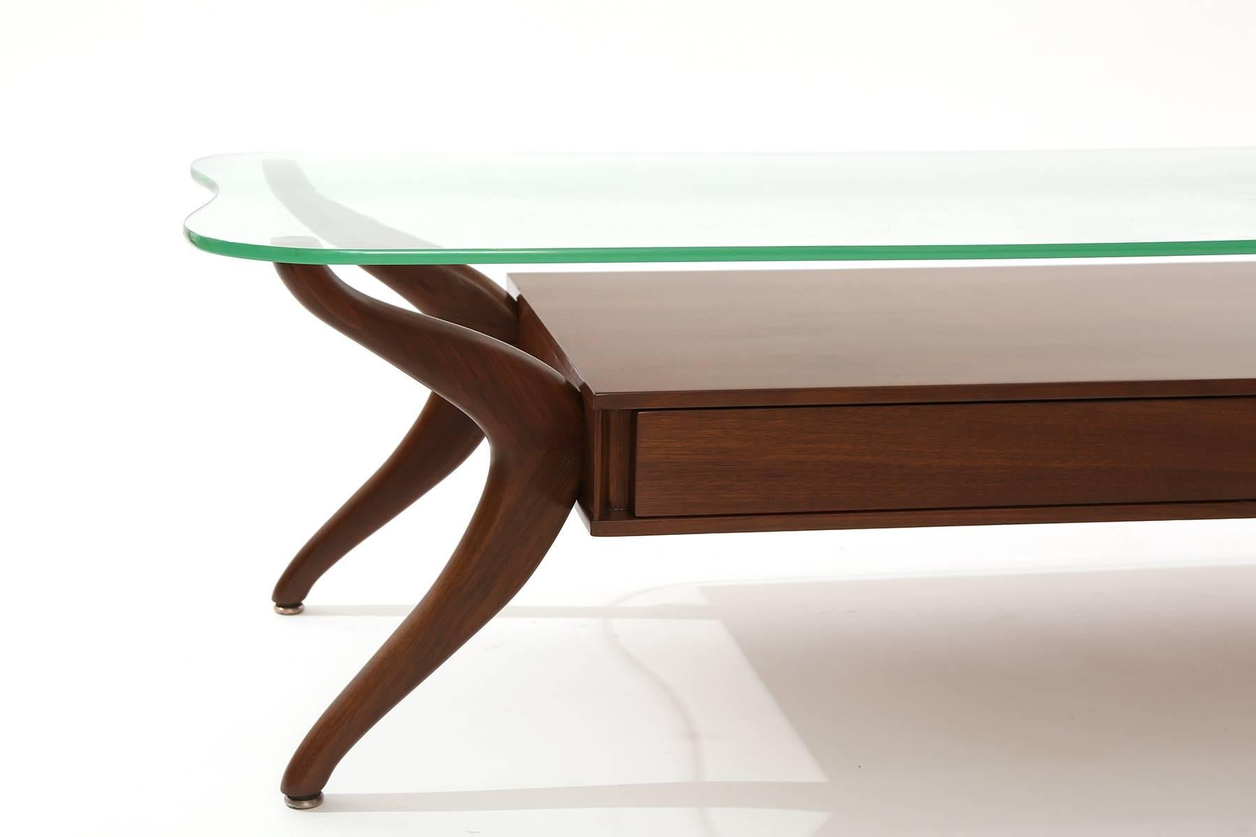 Free-form walnut and glass coffee table circa late 1950s. This example has solid walnut legs, two drawers for storage and free-form original glass top.
Newly finished.